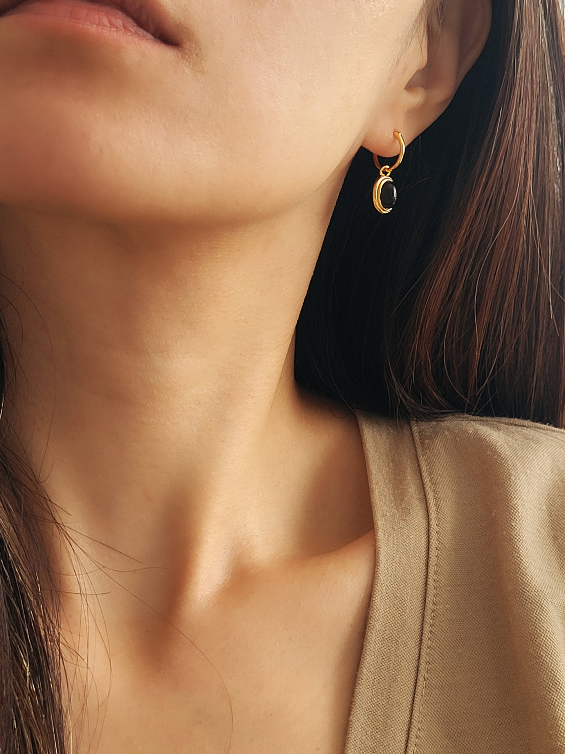 A woman wearing gold vermeil dangle earrings with an oval black onyx gemstone dressed in minimalist and elegant style