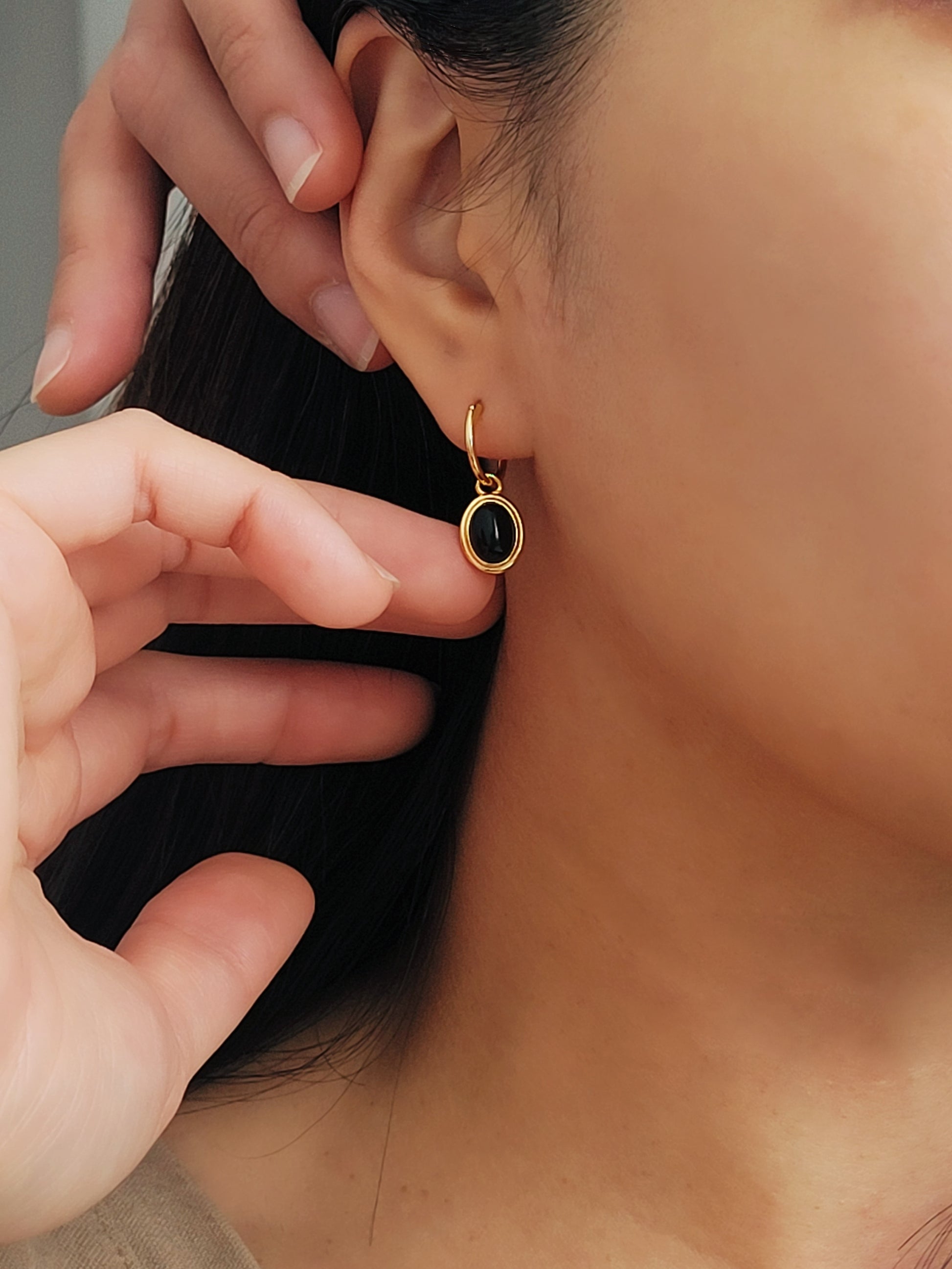 Close-up of an oval black onyx gemstone earring on model's ear