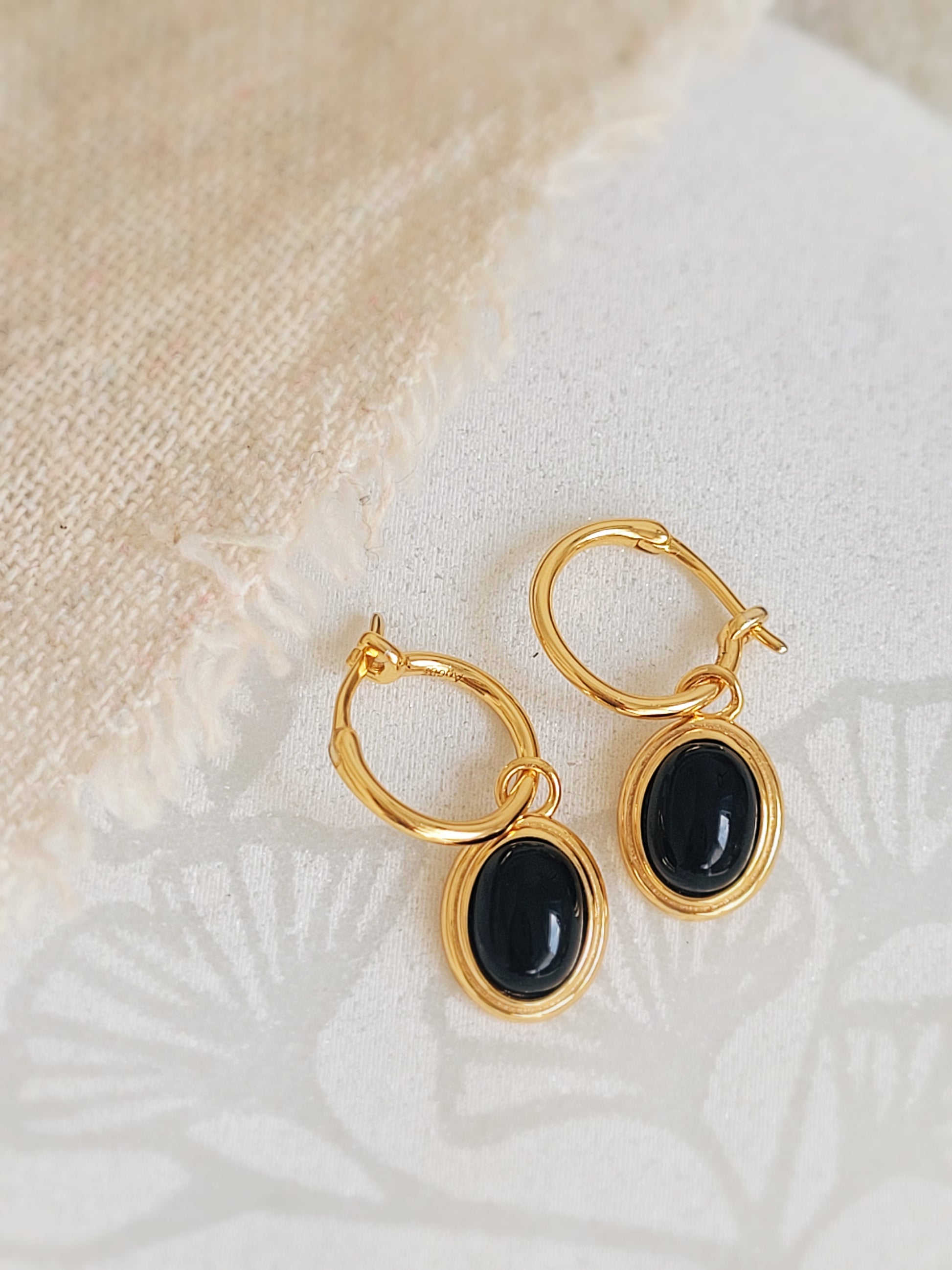 A pair of oval black onyx gemstone earrings on a white surface, showcasing its detailed craftsmanship