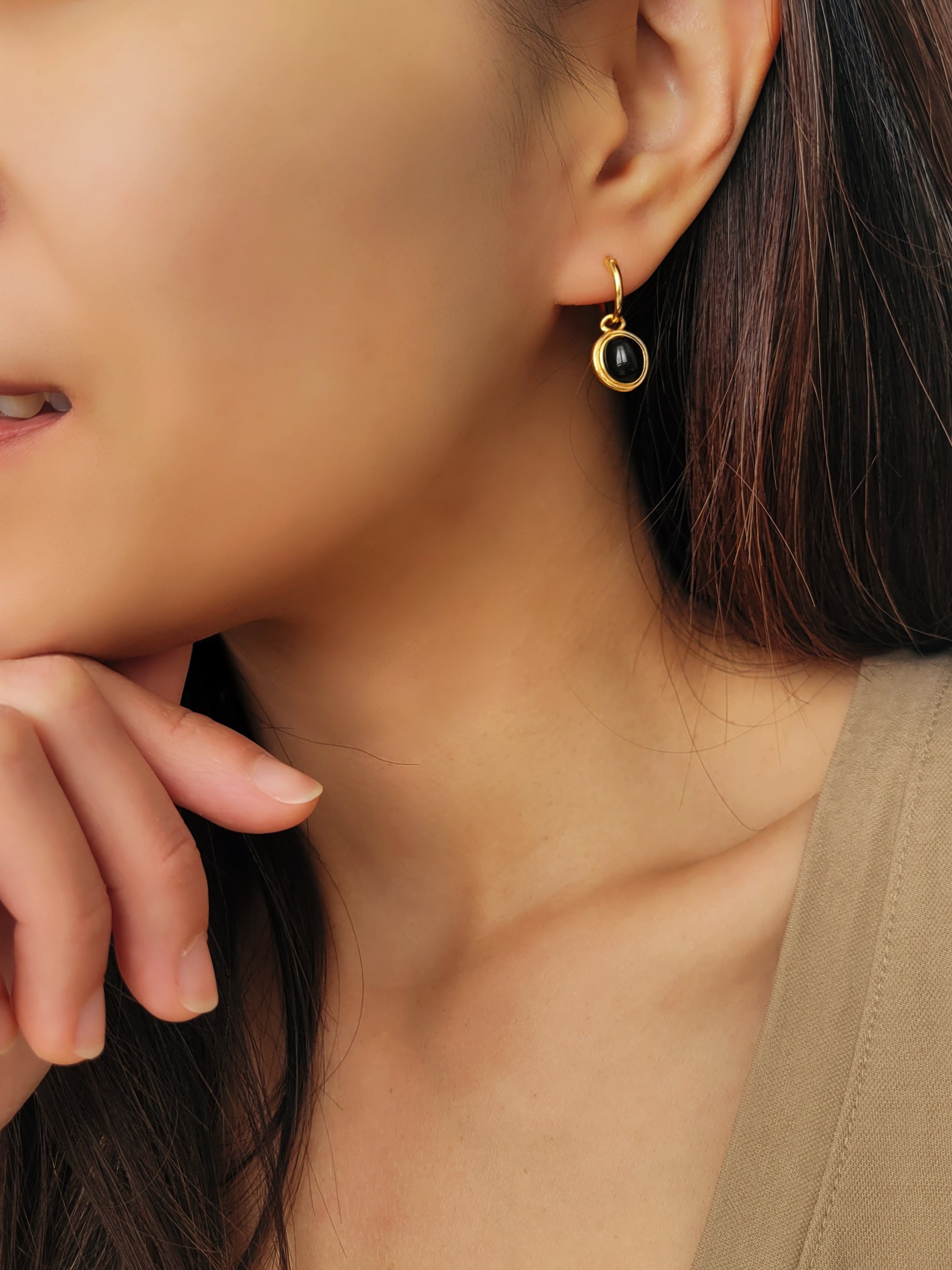 An elegant black and gold drop hoop earring worn on a woman's ear
