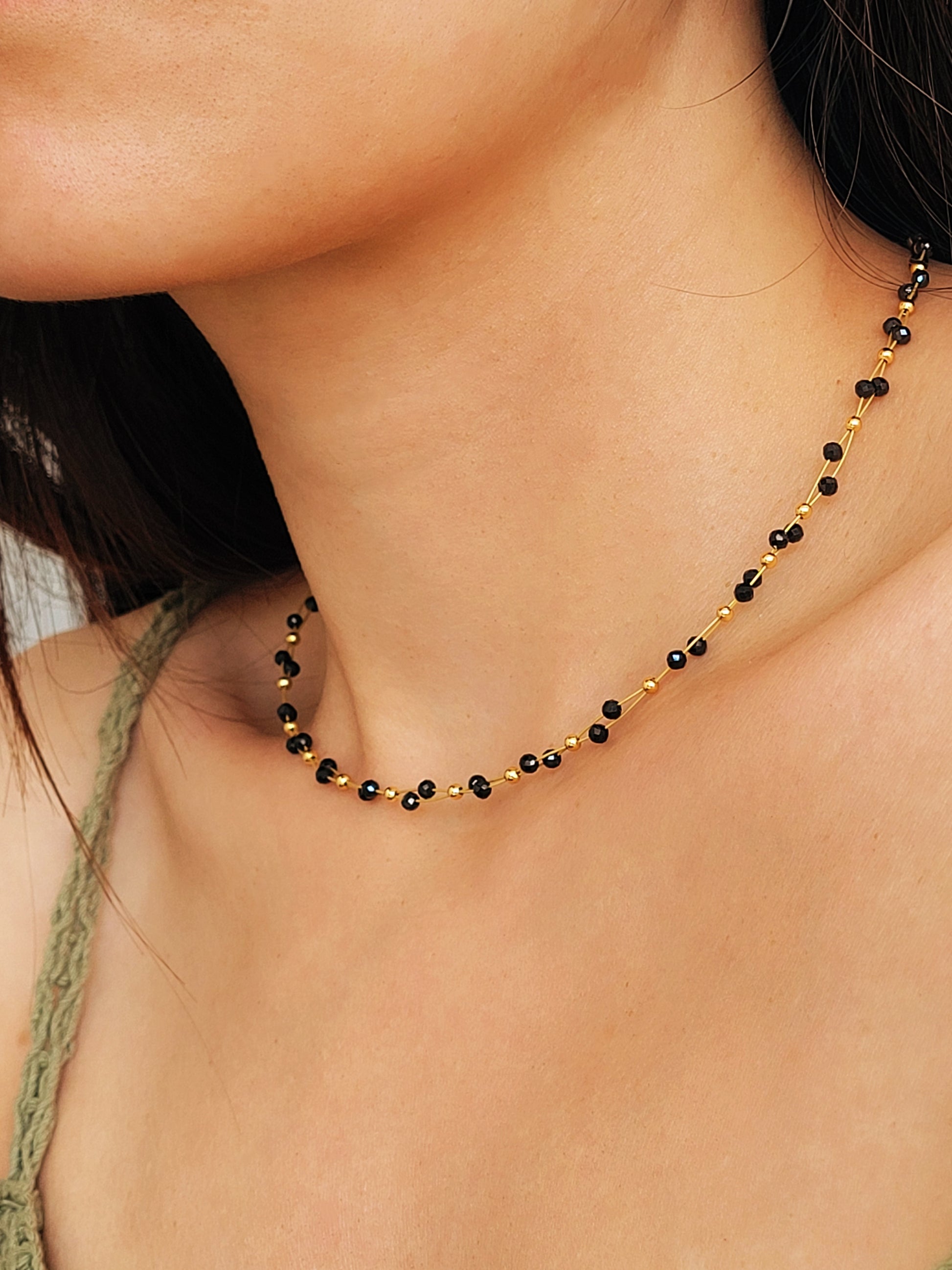Close-up of a woman wearing a black spinel beaded choker necklace with 22k gold accents, styled for minimalist everyday wear. Handmade in natural gemstone and gold plated sterling silver premium materials, perfect gift for anniversary, birthday or self care.