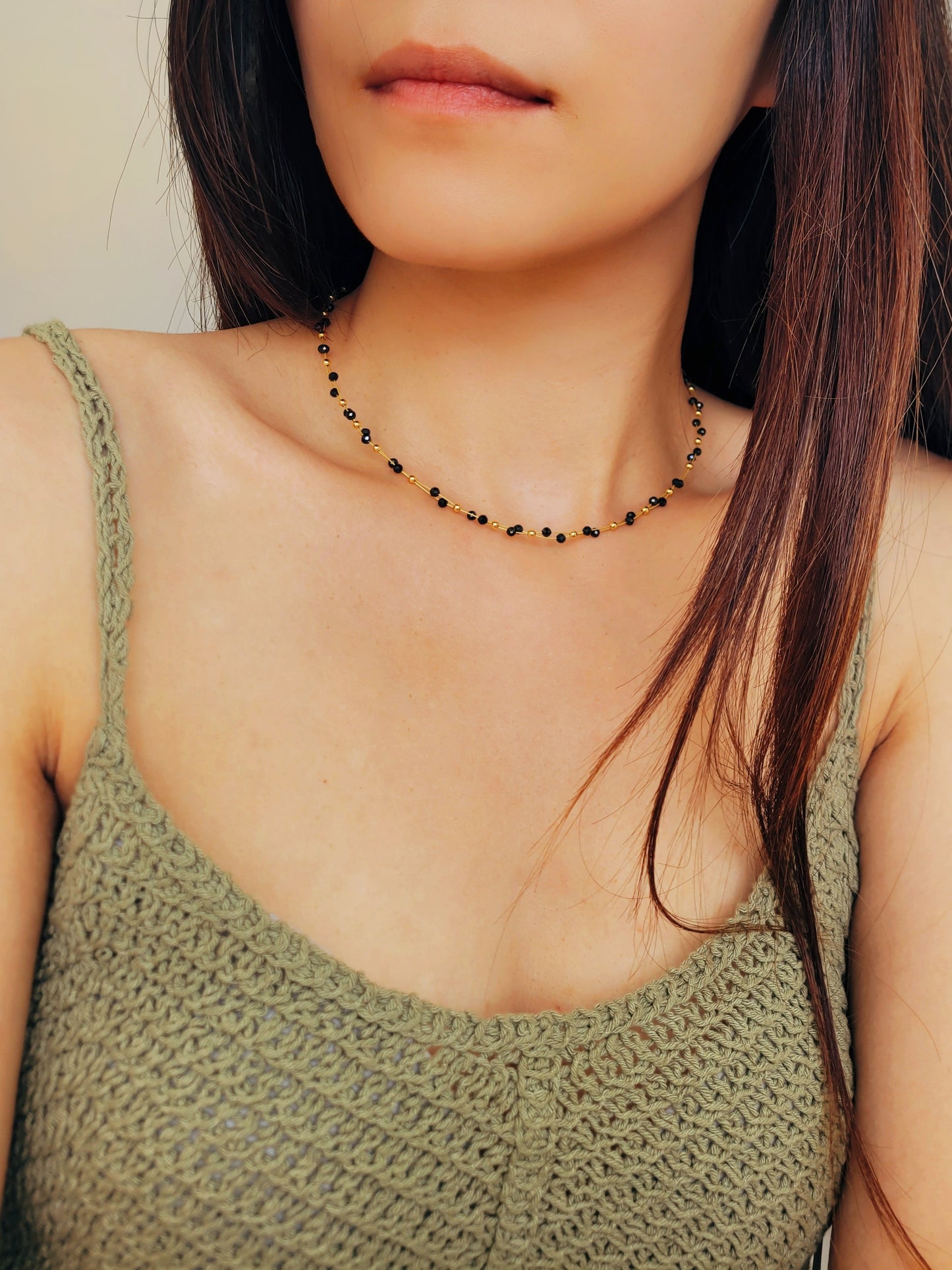 Close-up of a woman wearing a black spinel beaded choker necklace with 22k gold accents, styled for minimalist everyday wear. Handmade in natural gemstone and gold plated sterling silver premium materials, perfect gift for anniversary, birthday or self care.