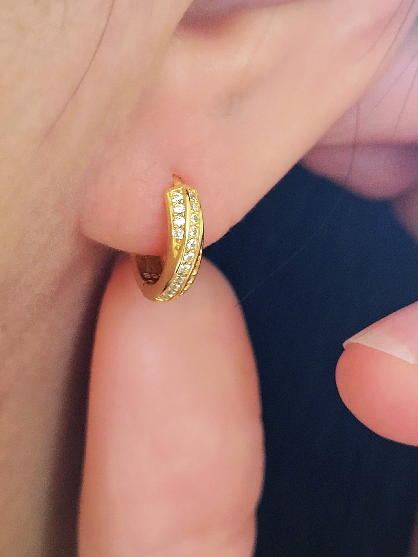 Close-up of a woman's ear wearing chic and understated gold crisscross hoop earrings. Emphasizing the minimalistic elegance of the jewelry.