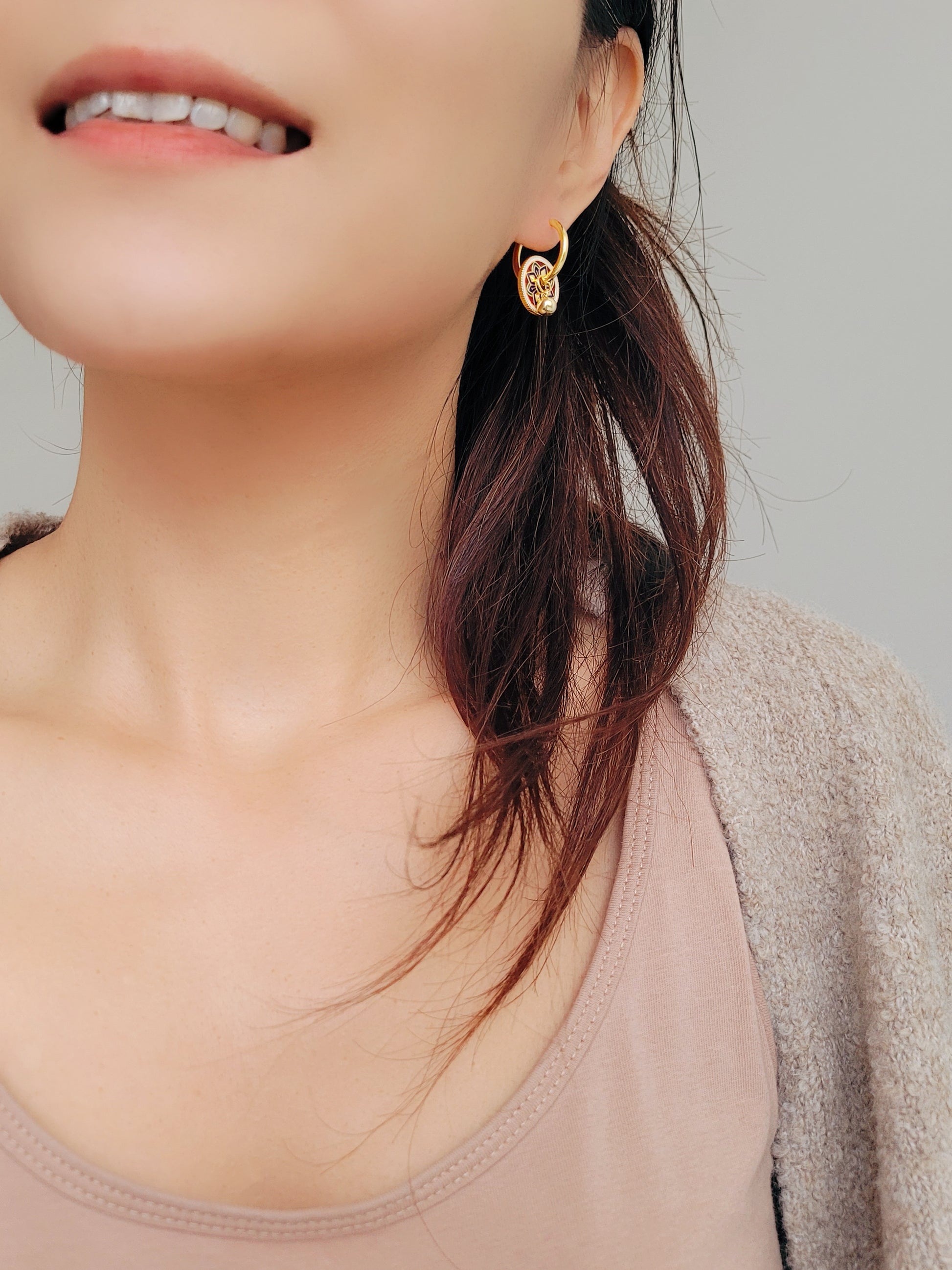 Gold hoop earrings featuring a tile pattern disc and a gold ball dangle, displayed on a white surface showcasing their elegant and unique artisan design.