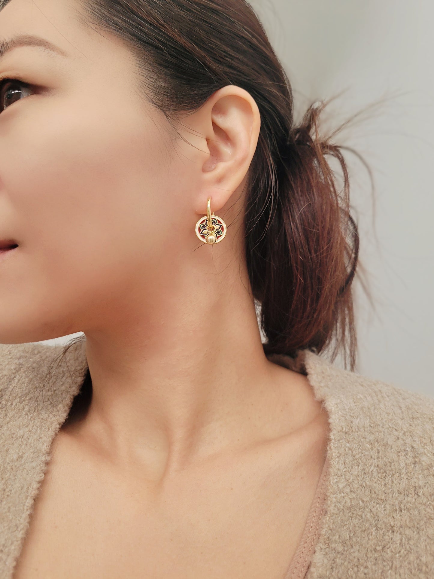 Gold hoop earrings featuring a tile pattern disc and a gold ball dangle, displayed on a white surface showcasing their elegant and unique artisan design.