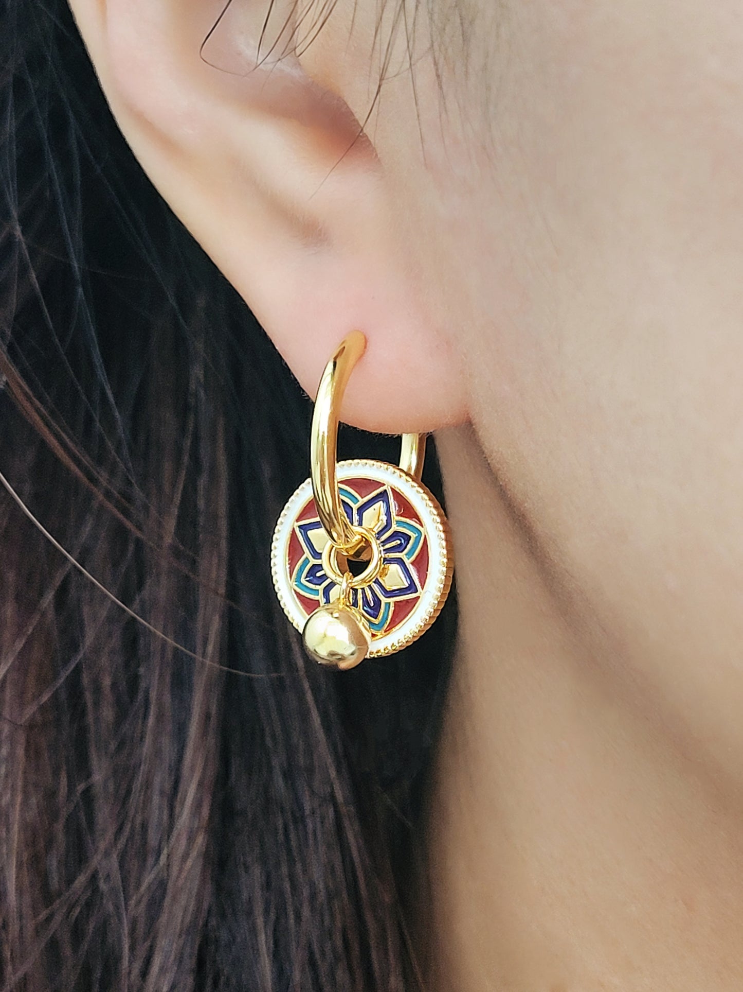 Gold hoop earrings featuring a tile pattern disc and a gold ball dangle, displayed on a white surface showcasing their elegant and unique artisan design.