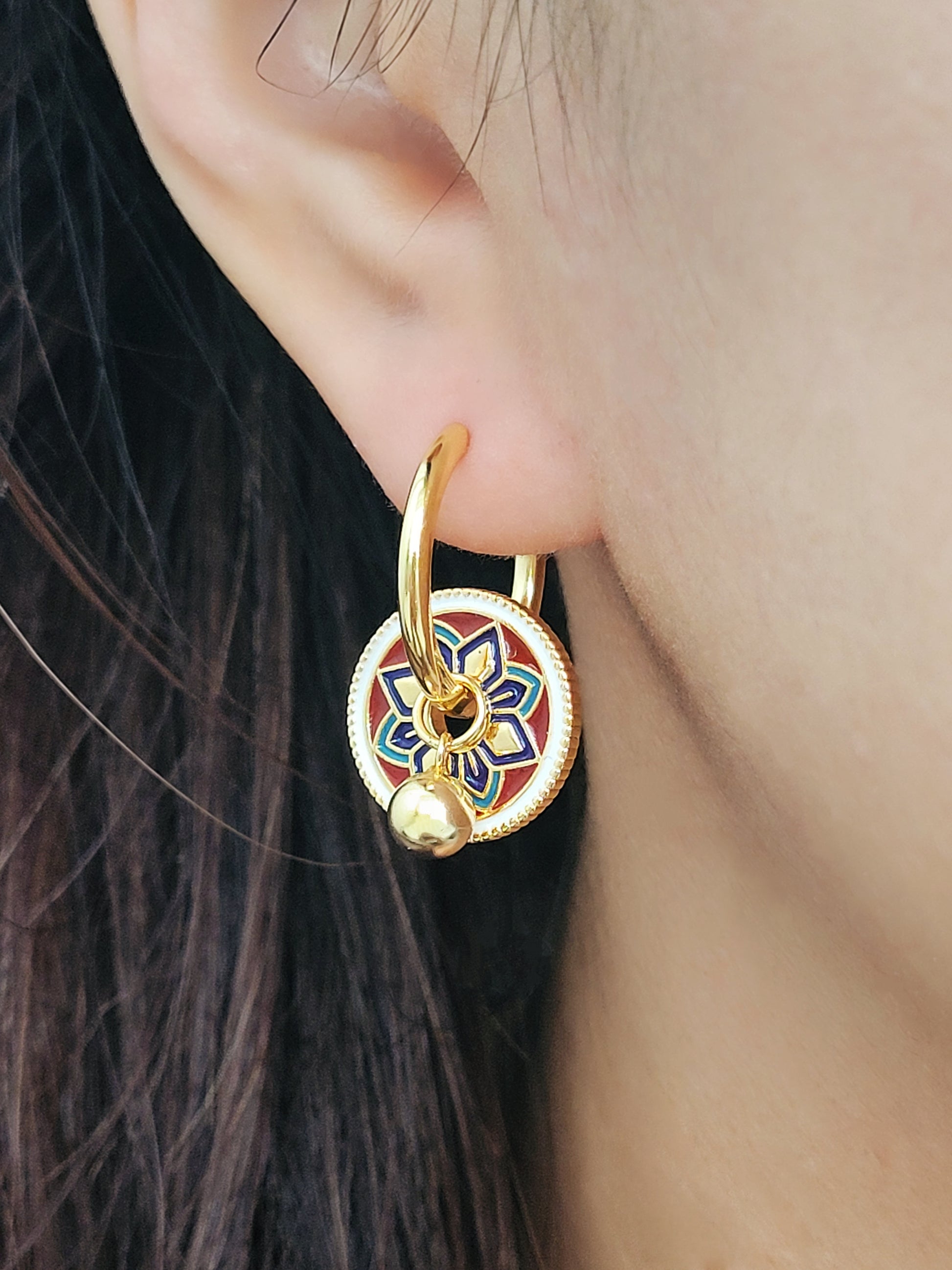Gold hoop earrings featuring a tile pattern disc and a gold ball dangle, displayed on a white surface showcasing their elegant and unique artisan design.
