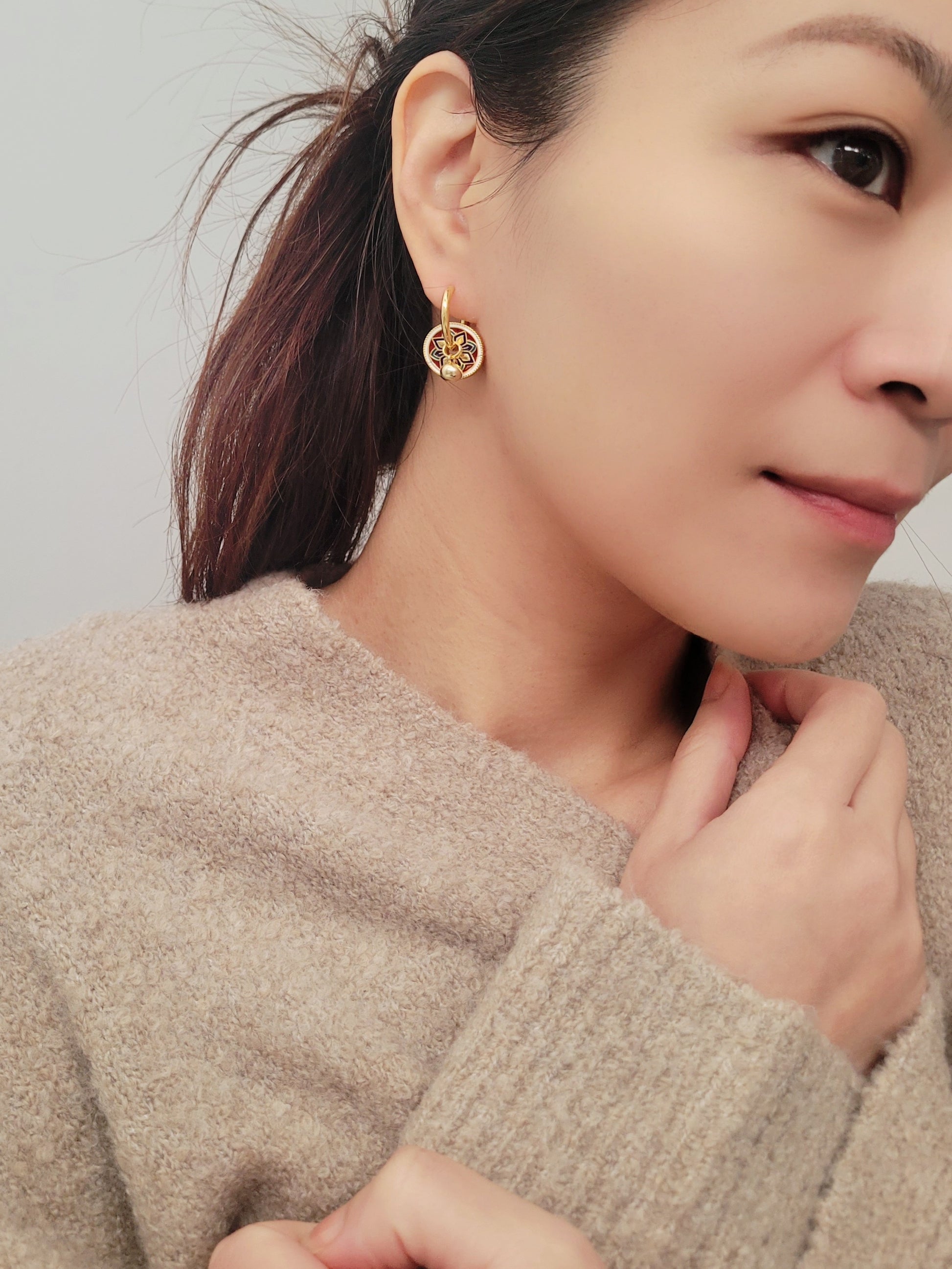 Gold hoop earrings featuring a tile pattern disc and a gold ball dangle, displayed on a white surface showcasing their elegant and unique artisan design.