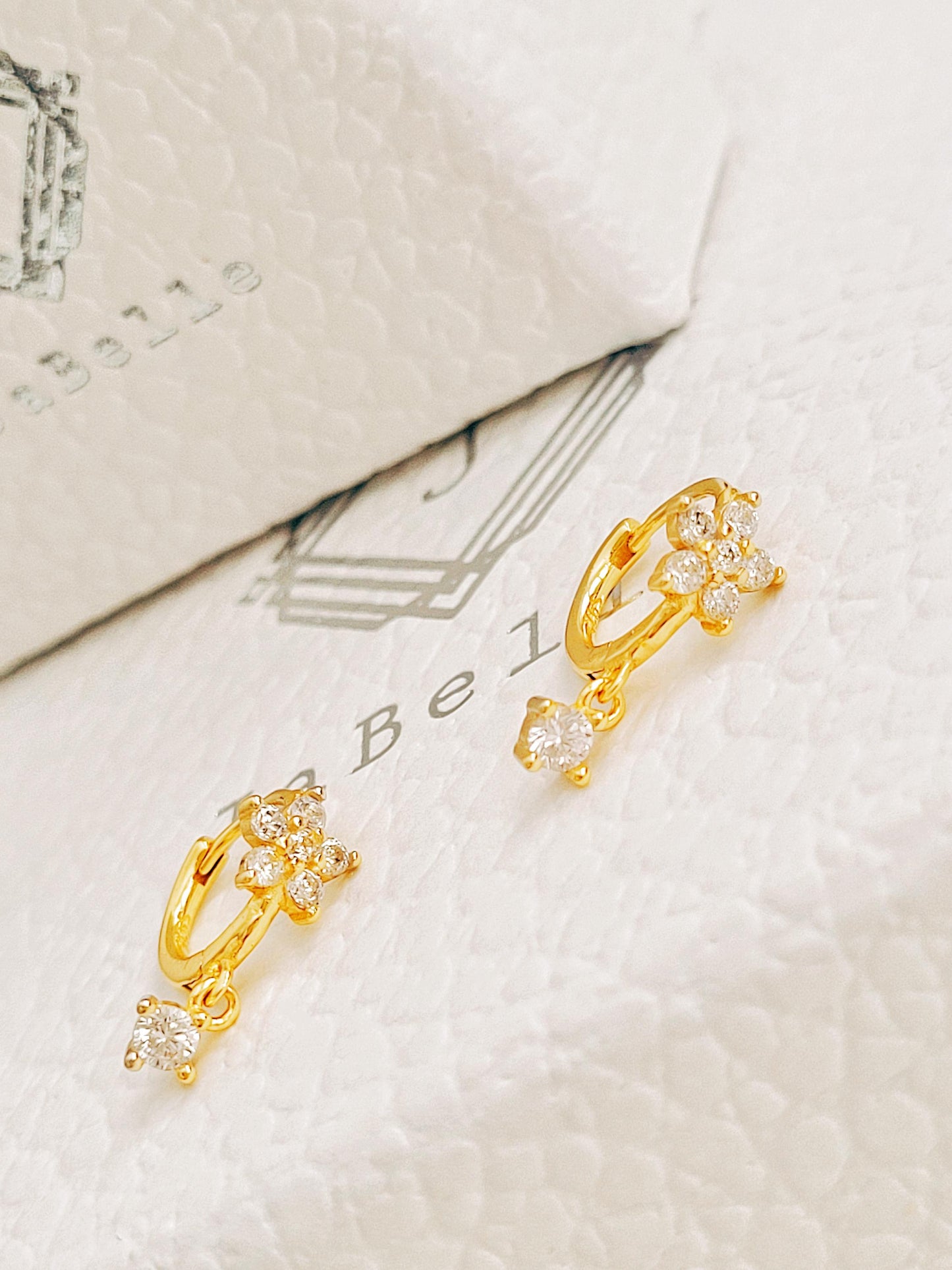 Gold flower huggie earrings with clear stones on a textured white surface