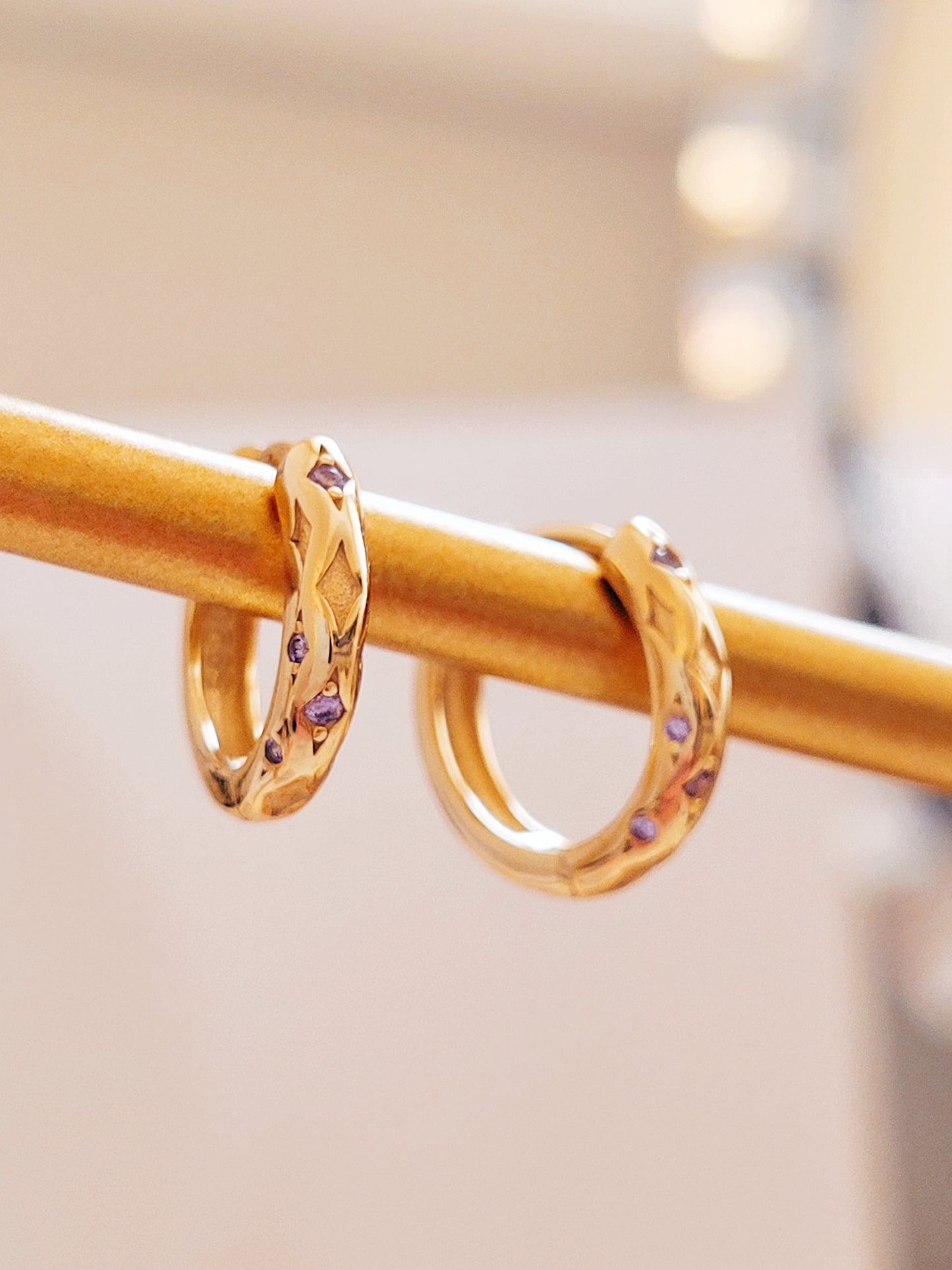 Close up of 18k gold plated sterling silver huggie hoop earrings with purple cubic zirconia crystals, featuring a cosmic star inspired design.