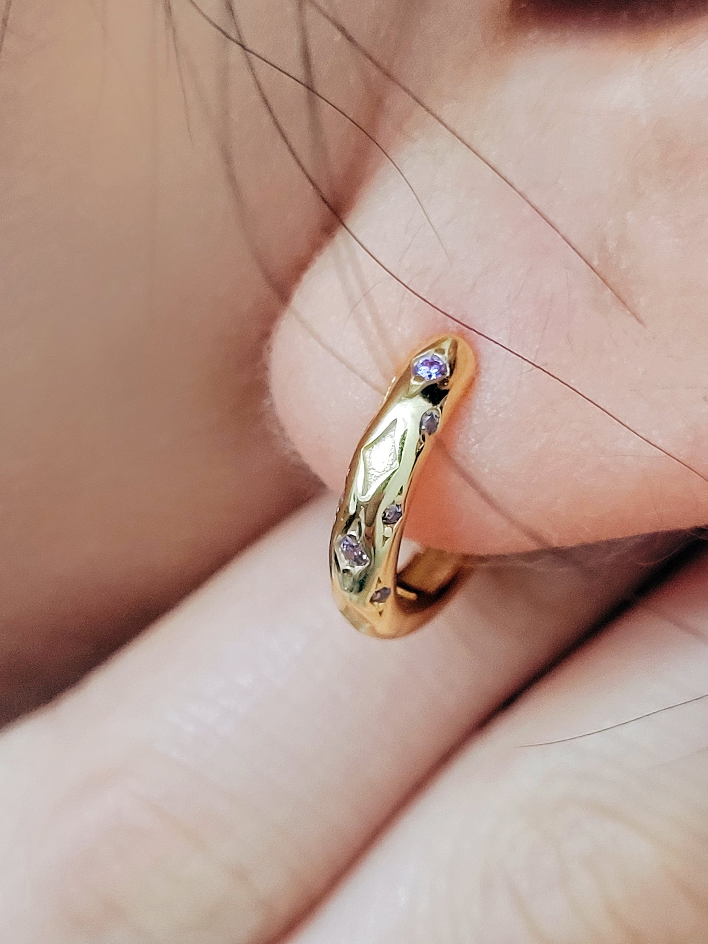 Close up of a woman wearing 18k gold plated sterling silver huggie hoop earrings with purple crystals, featuring a cosmic star inspired design.