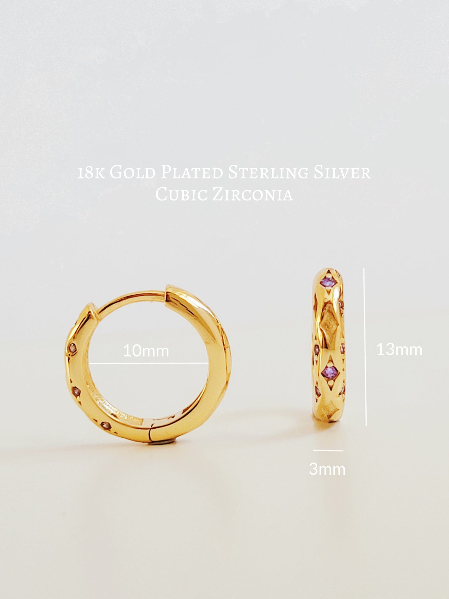 Close up of 18k gold plated sterling silver huggie hoop earrings with purple cubic zirconia crystals, featuring a cosmic star inspired design.