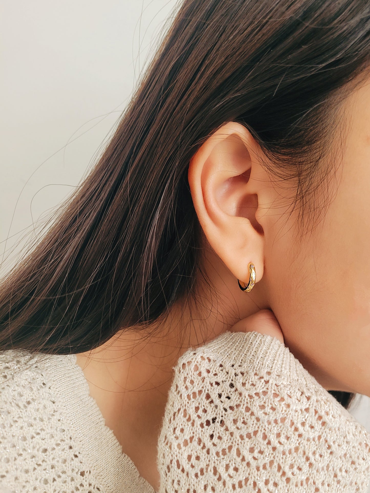 Close up of a woman wearing 18k gold plated sterling silver huggie hoop earrings with purple crystals, featuring a cosmic star inspired design.