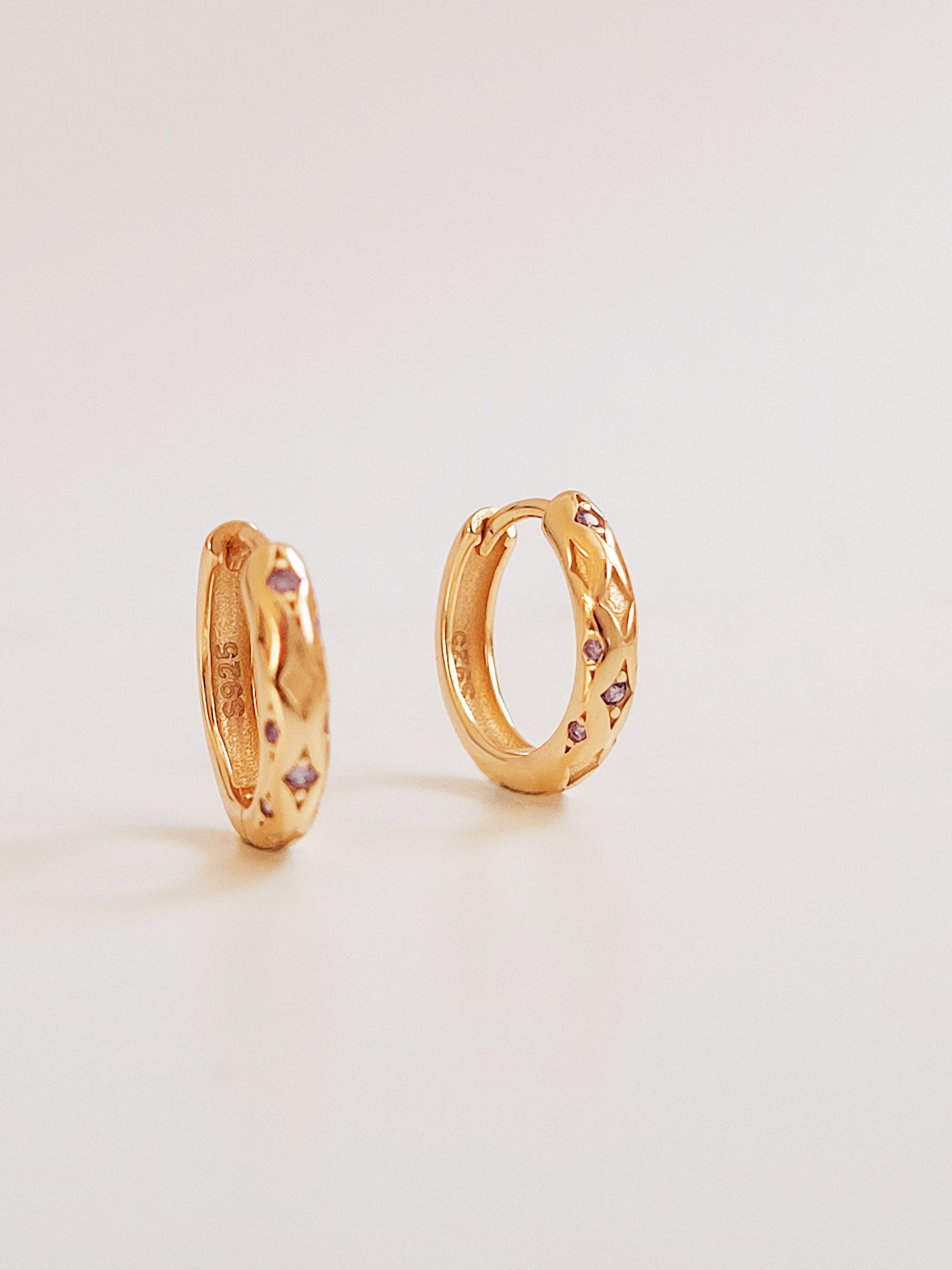 Close up of 18k gold plated sterling silver huggie hoop earrings with purple cubic zirconia crystals, featuring a cosmic star inspired design.