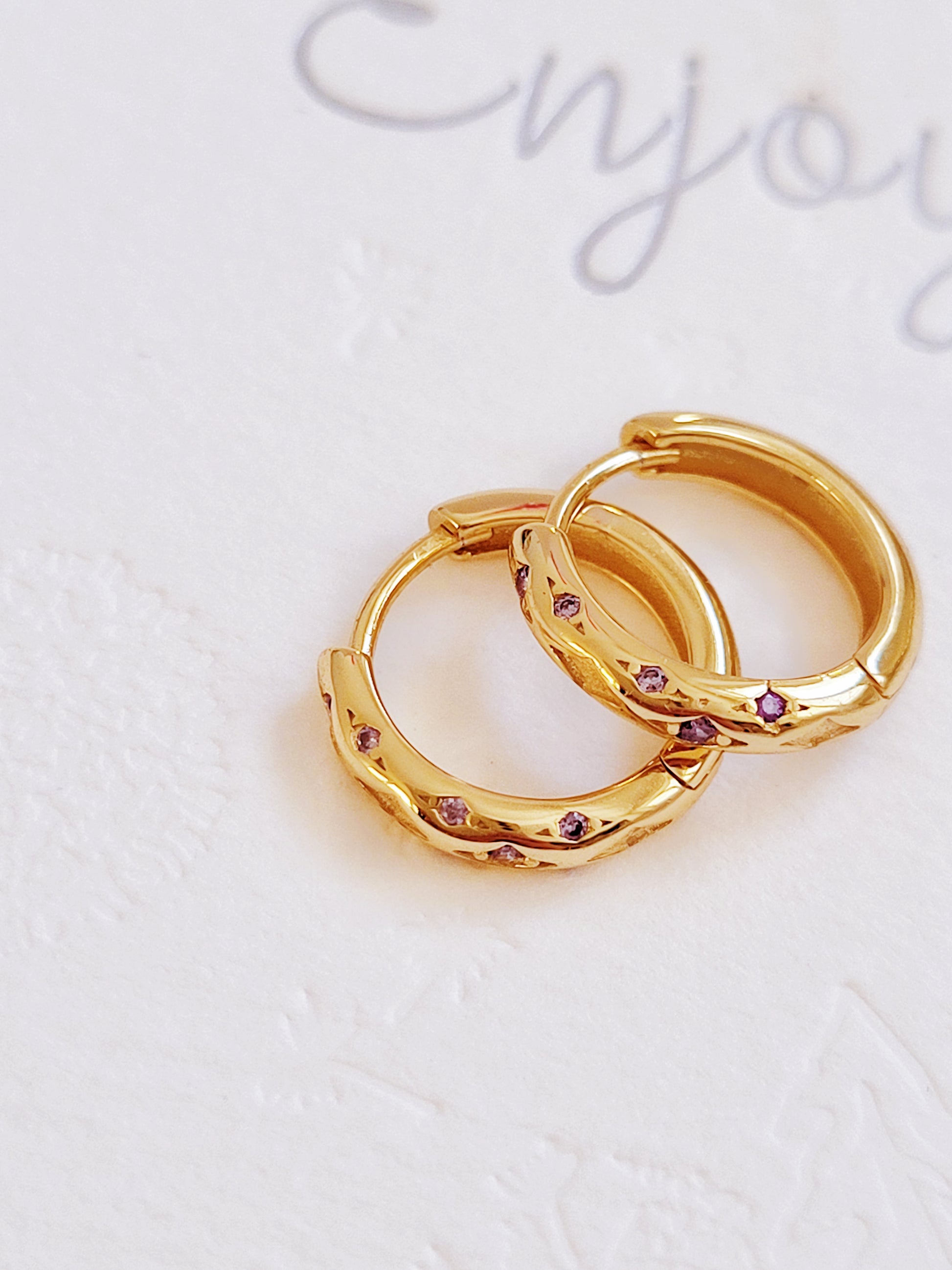 Close up of 18k gold plated sterling silver huggie hoop earrings with purple cubic zirconia crystals, featuring a cosmic star inspired design.