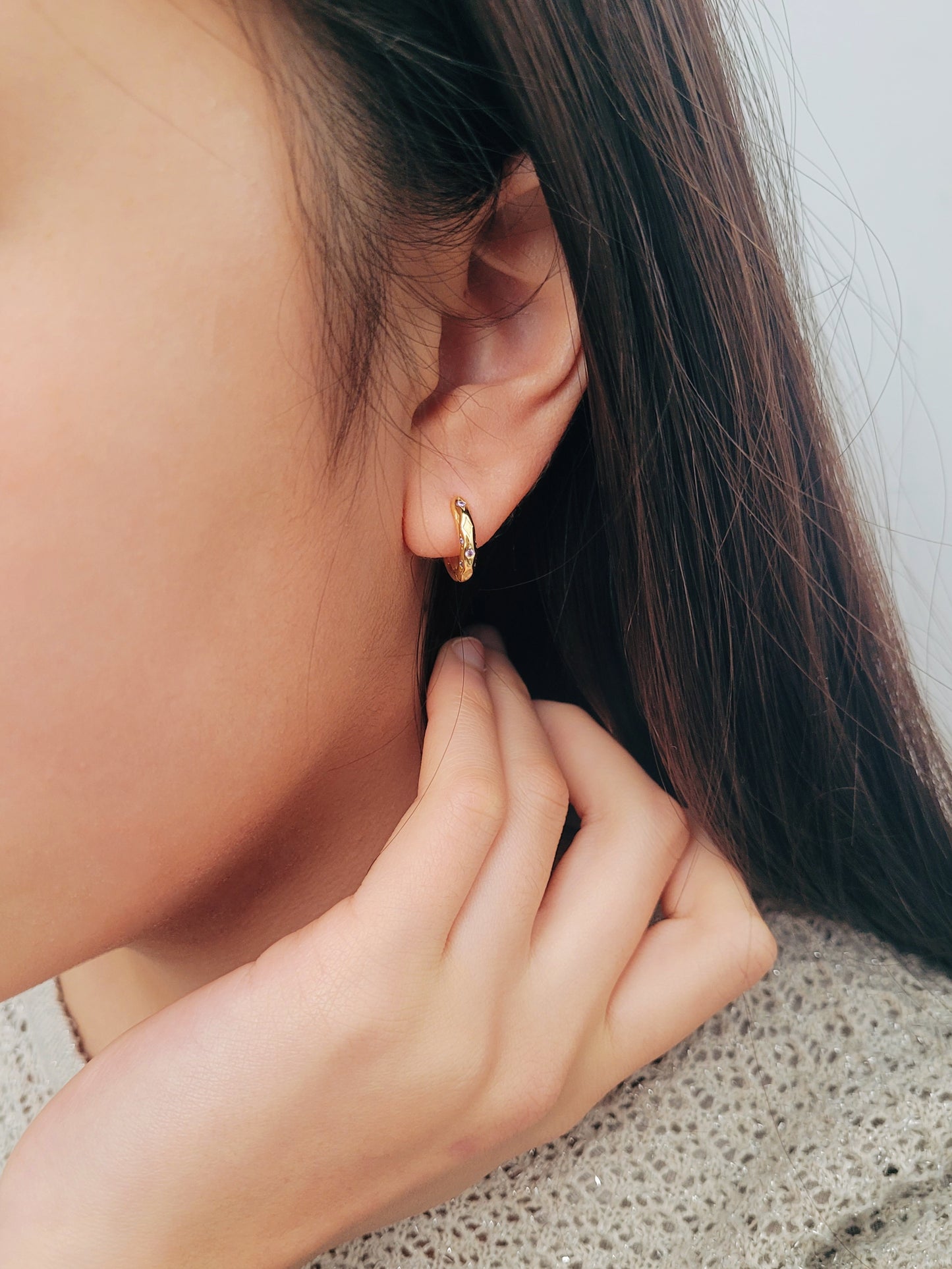 Close up of a woman wearing 18k gold plated sterling silver huggie hoop earrings with purple crystals, featuring a cosmic star inspired design.