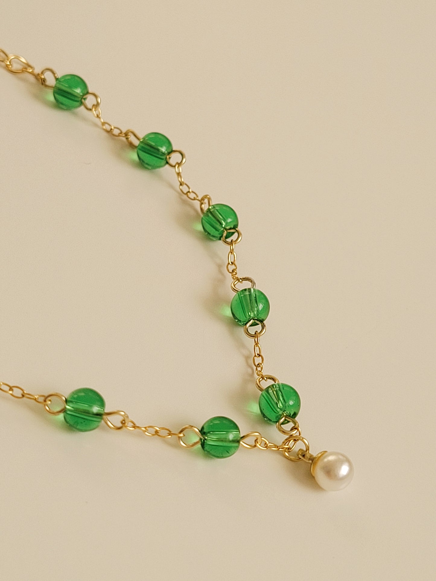 Elegant gold chain bracelet with green gemstone beads and a dainty pearl drop, perfect for a minimalist look.