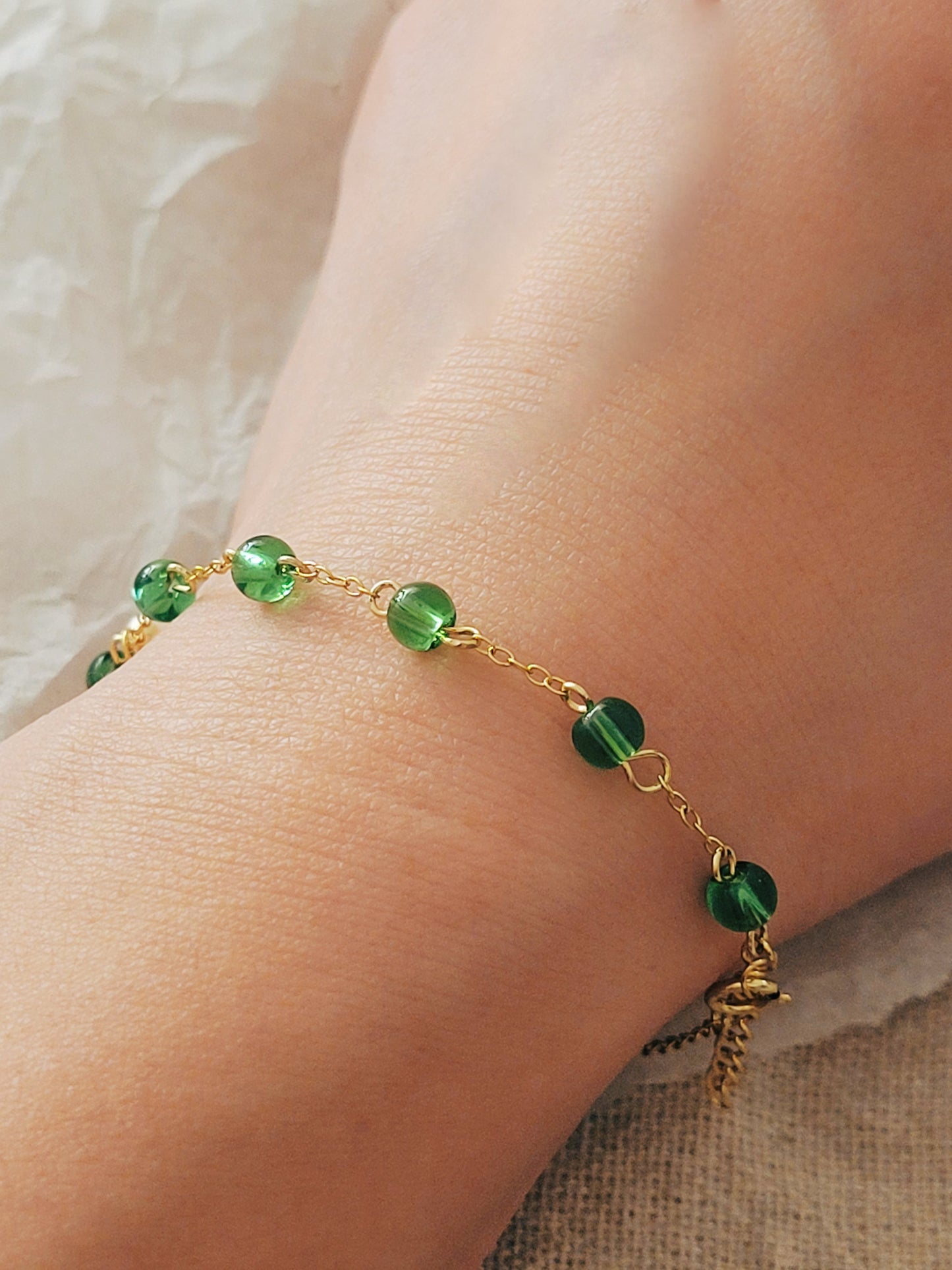 Elegant gold chain bracelet with green gemstone beads and a dainty pearl drop, perfect for a minimalist look.