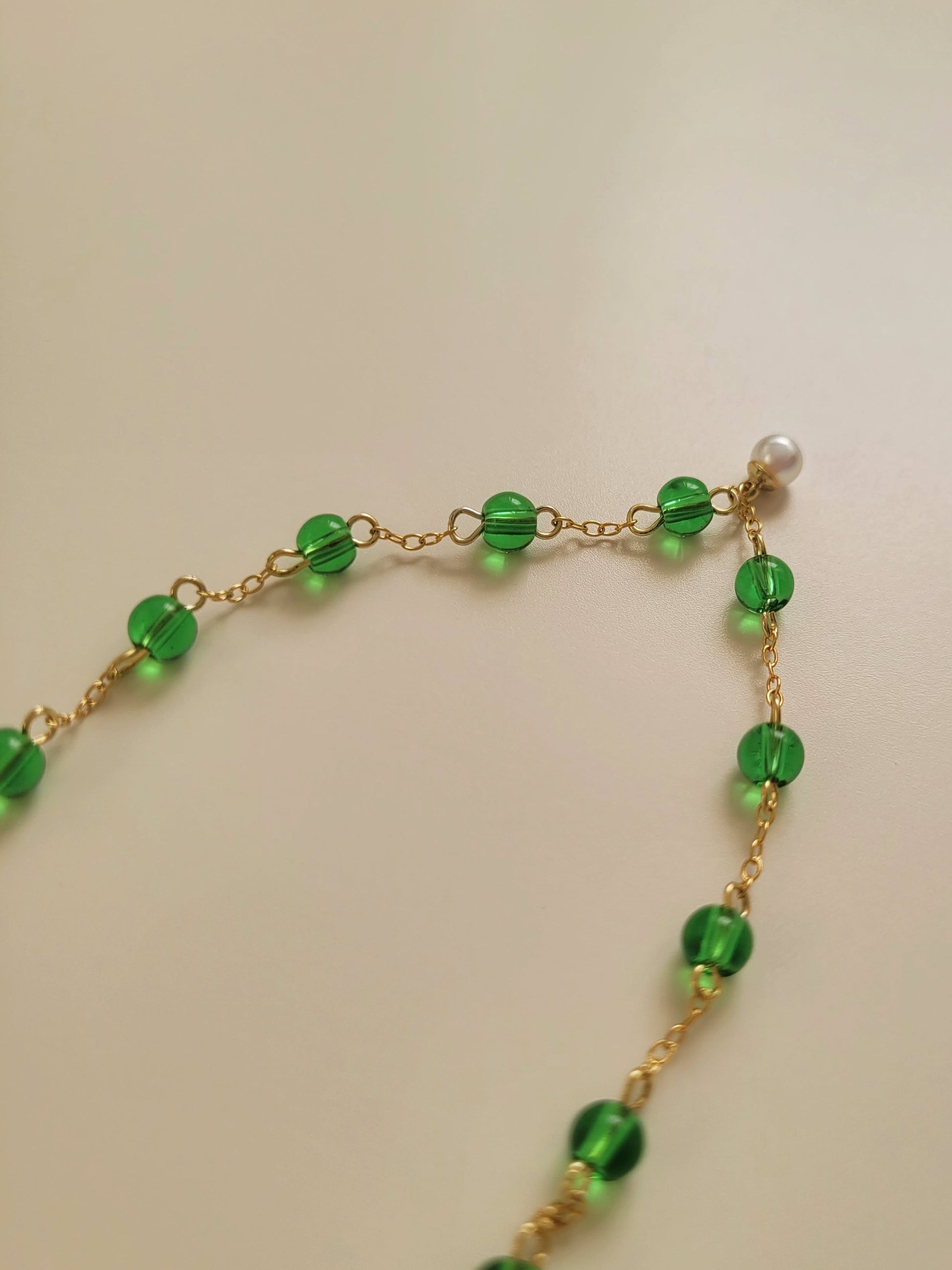 Elegant gold chain bracelet with green gemstone beads and a dainty pearl drop, perfect for a minimalist look.