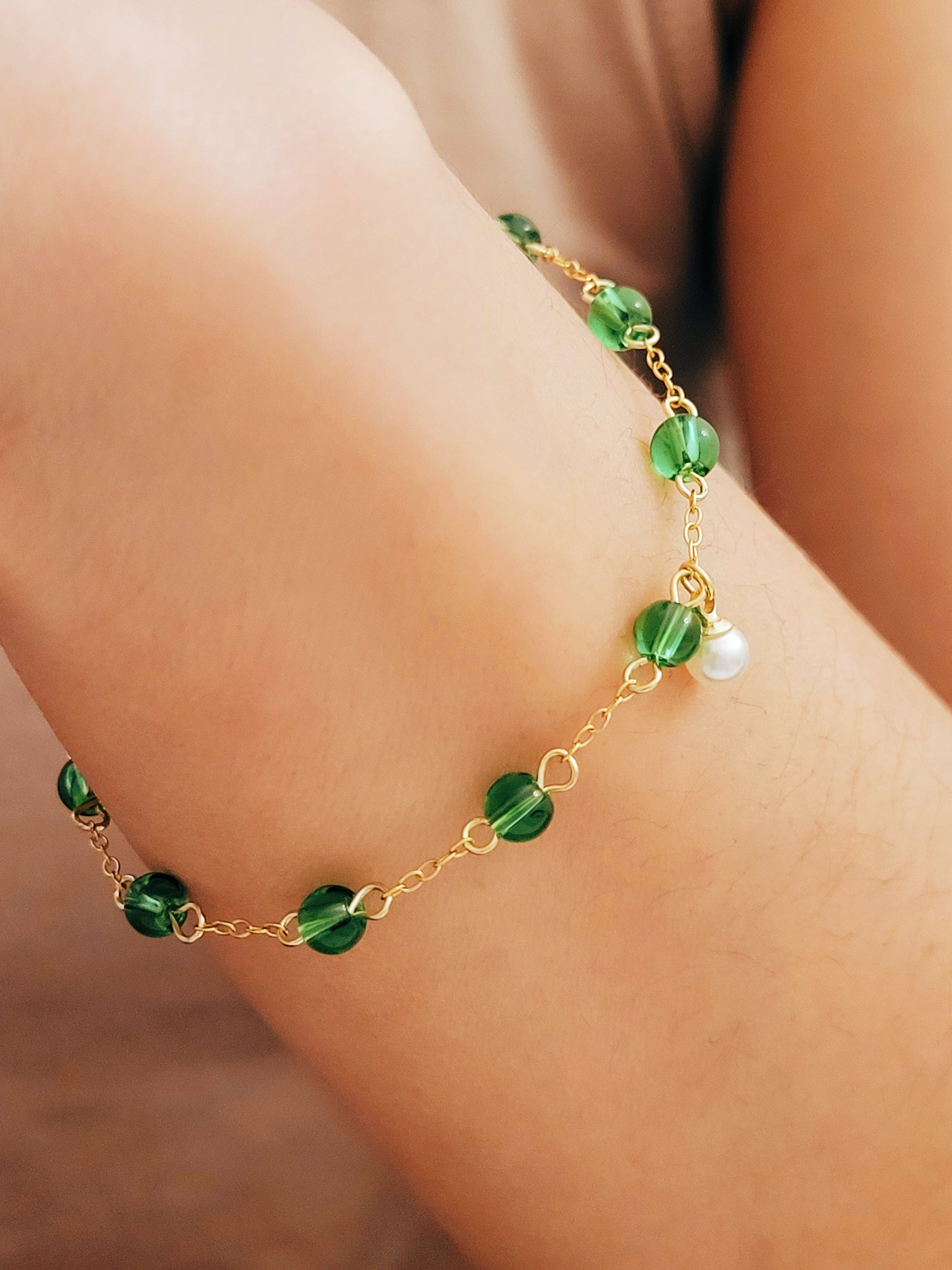 Elegant gold chain bracelet with green gemstone beads and a dainty pearl drop, perfect for a minimalist look.
