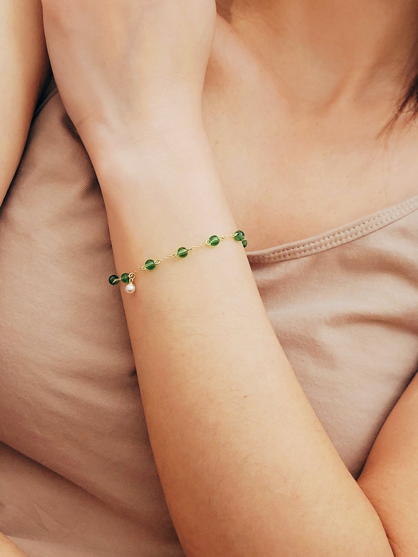 Elegant gold chain bracelet with green gemstone beads and a dainty pearl drop, perfect for a minimalist look.
