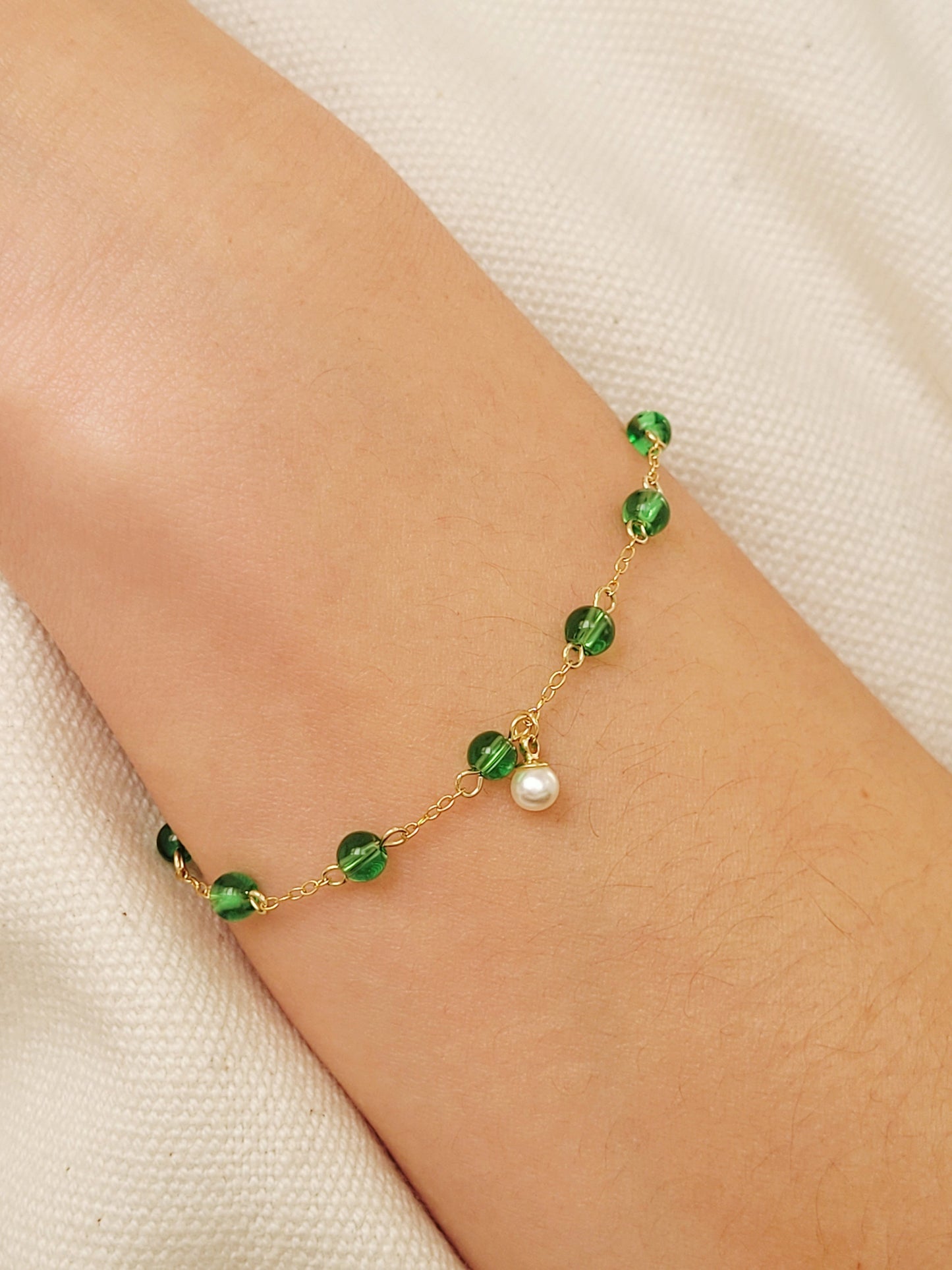 Elegant gold chain bracelet with green gemstone beads and a dainty pearl drop, perfect for a minimalist look.