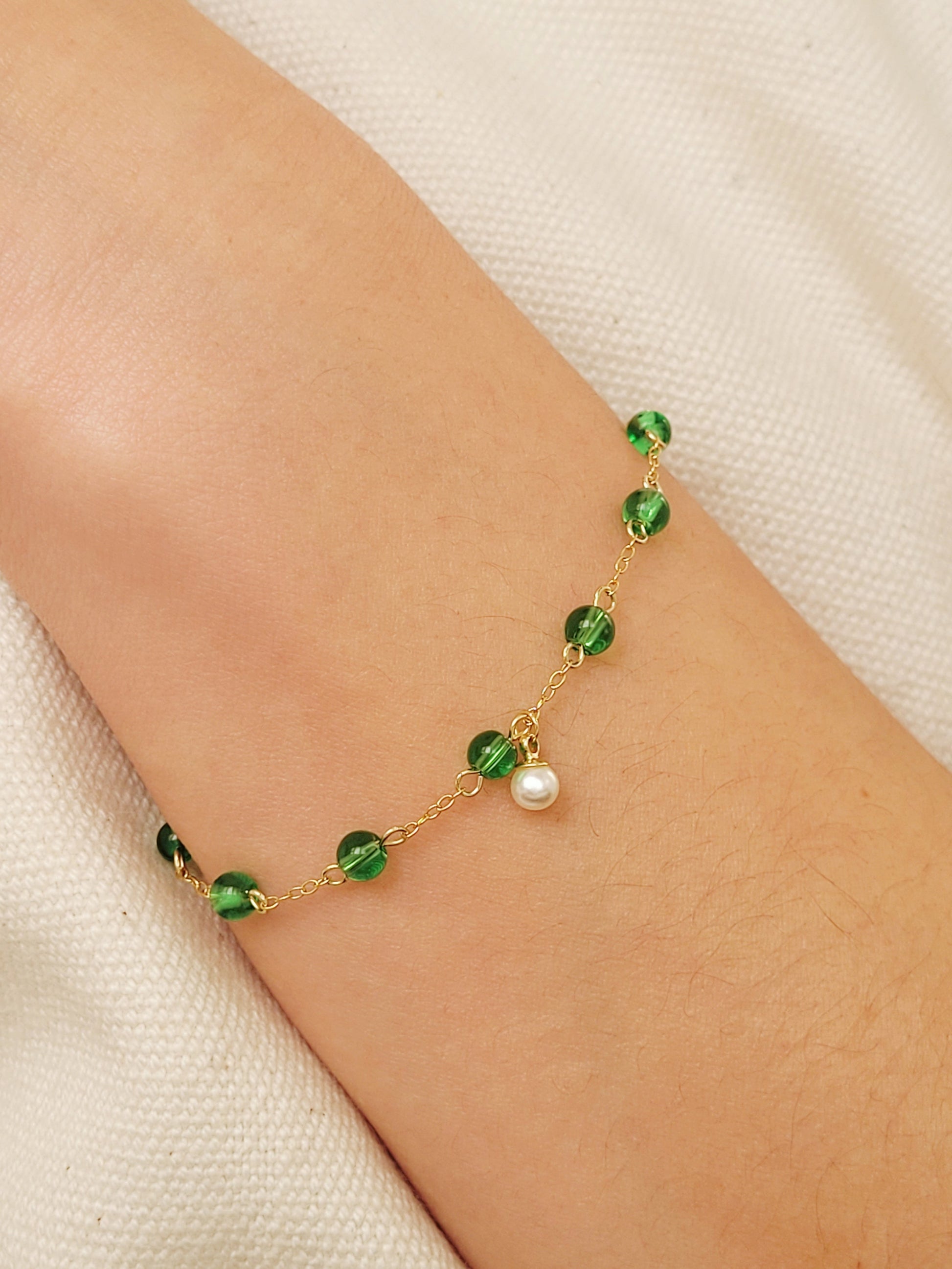 Elegant gold chain bracelet with green gemstone beads and a dainty pearl drop, perfect for a minimalist look.