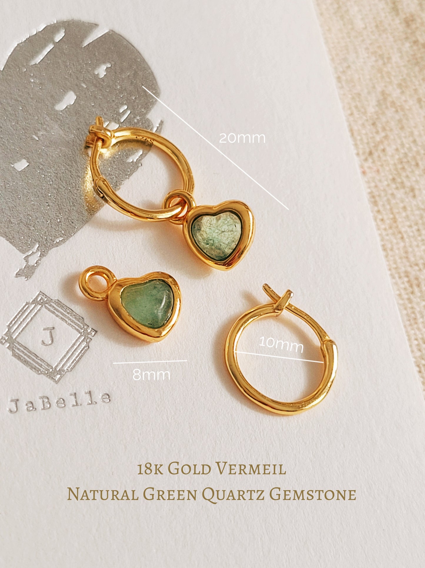 Gold hoop earrings with green crystal quartz on a textured surface