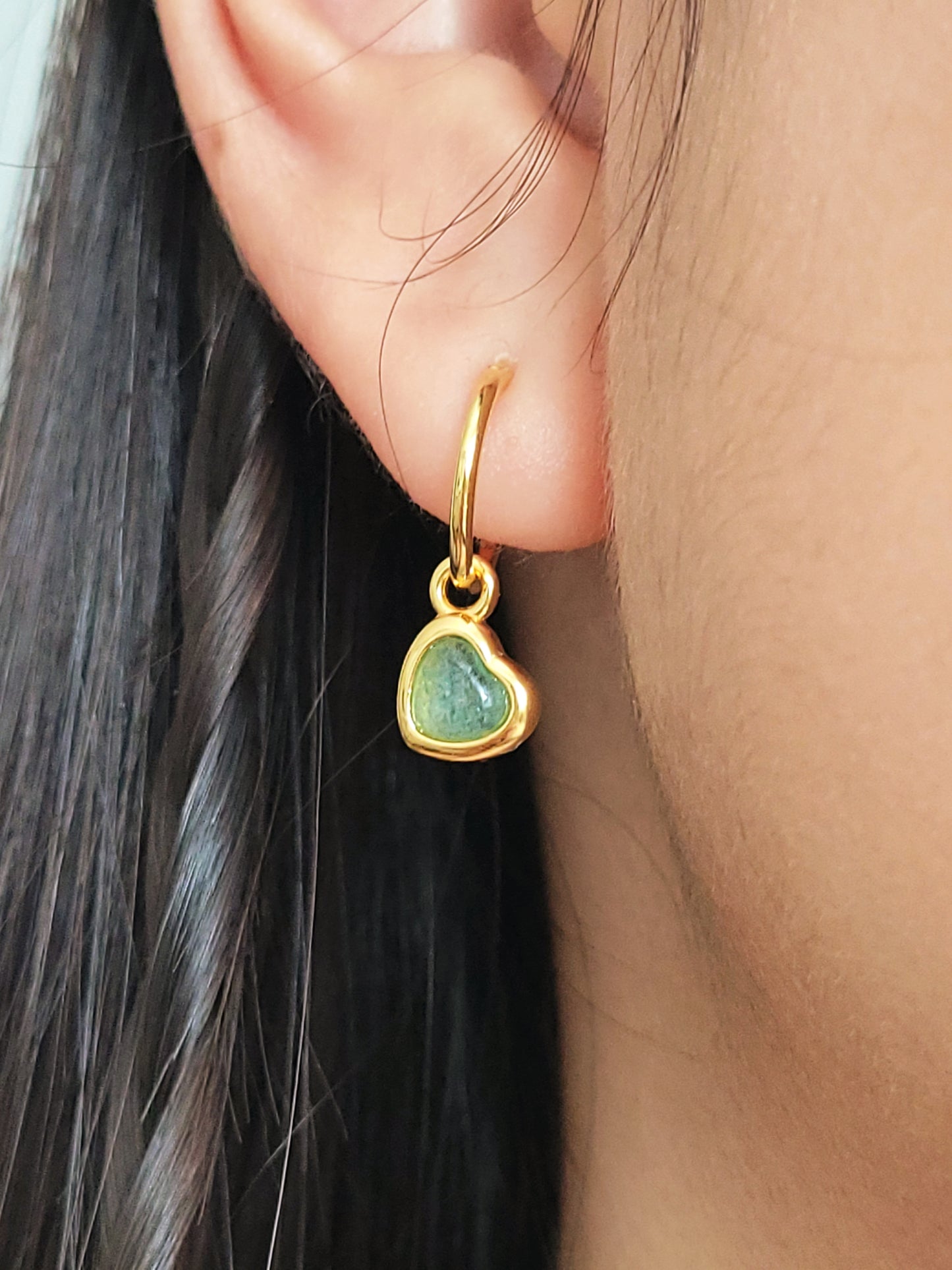 Gold heart dangle earring with a green gemstone worn by a person