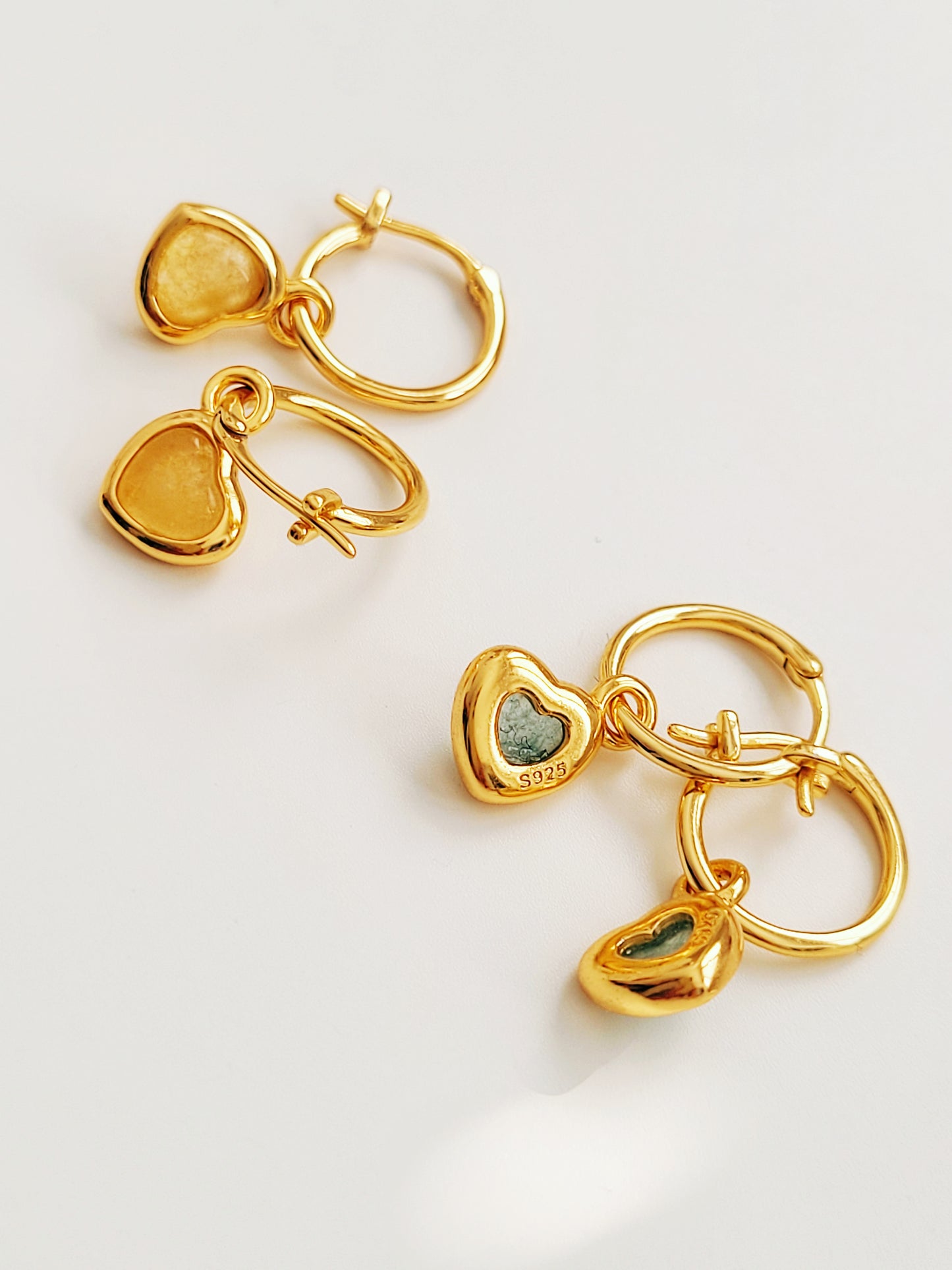 Gold heart shaped earrings with green stones on a light background