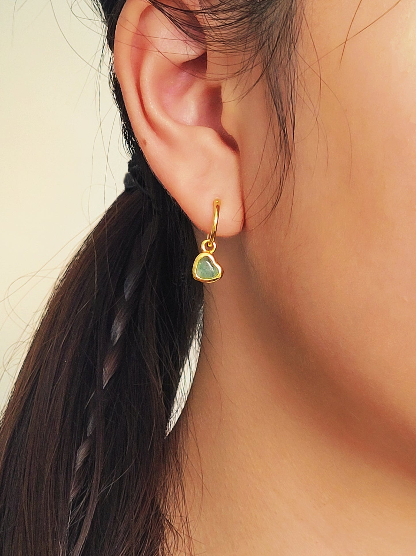 Cute gold heart earring with a green gemstone worn by a woman