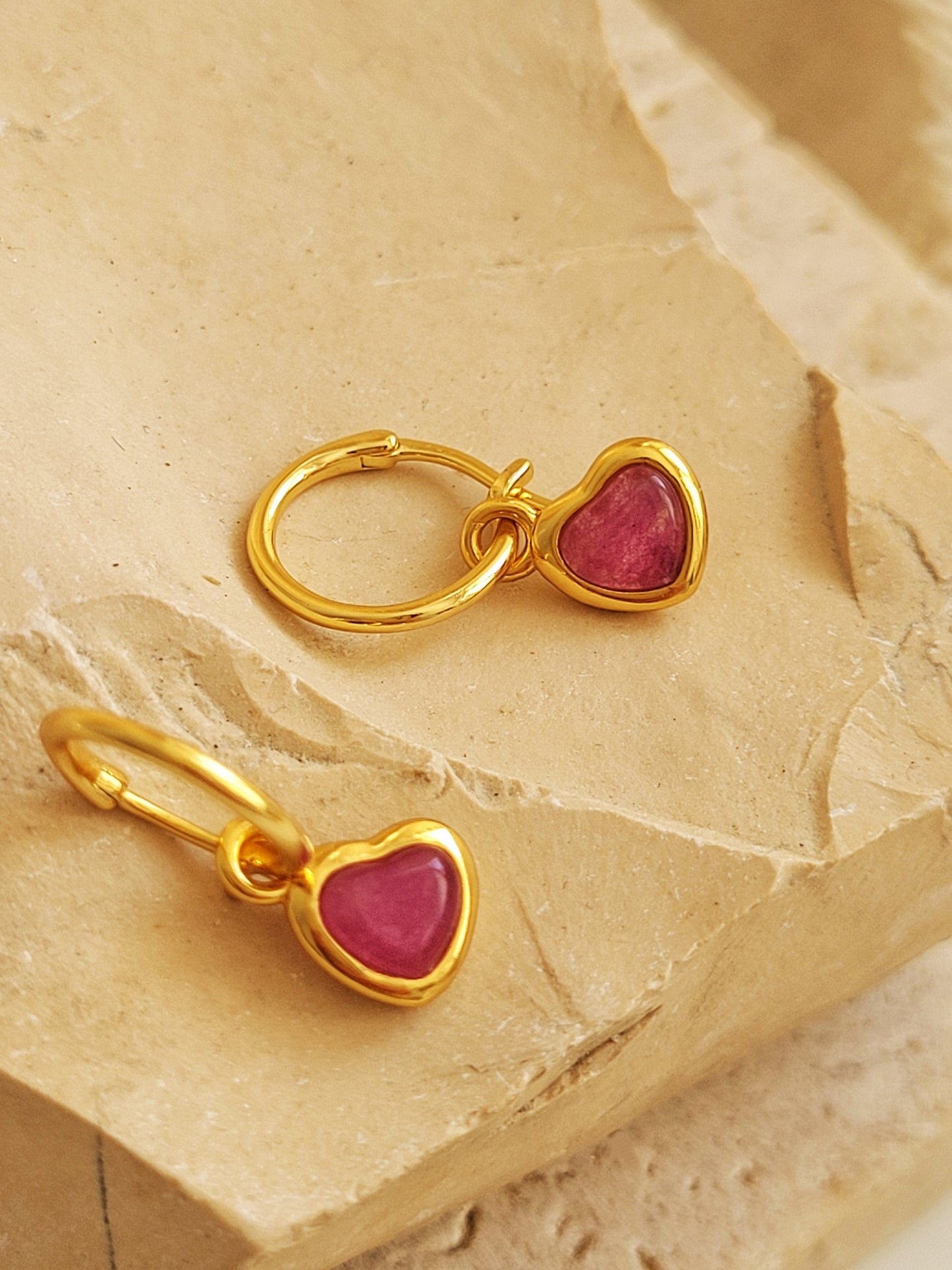 A pair of gold hoop earrings with heart dangle displayed on a stone surface