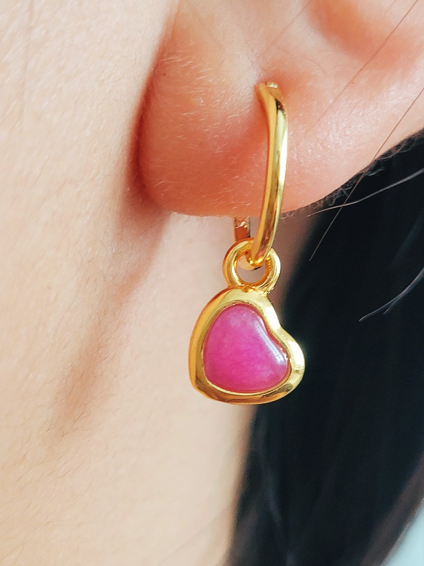 Close up of a woman wearing pink heart earrings crafted in gold plated sterling silver and natural quartz gemstone