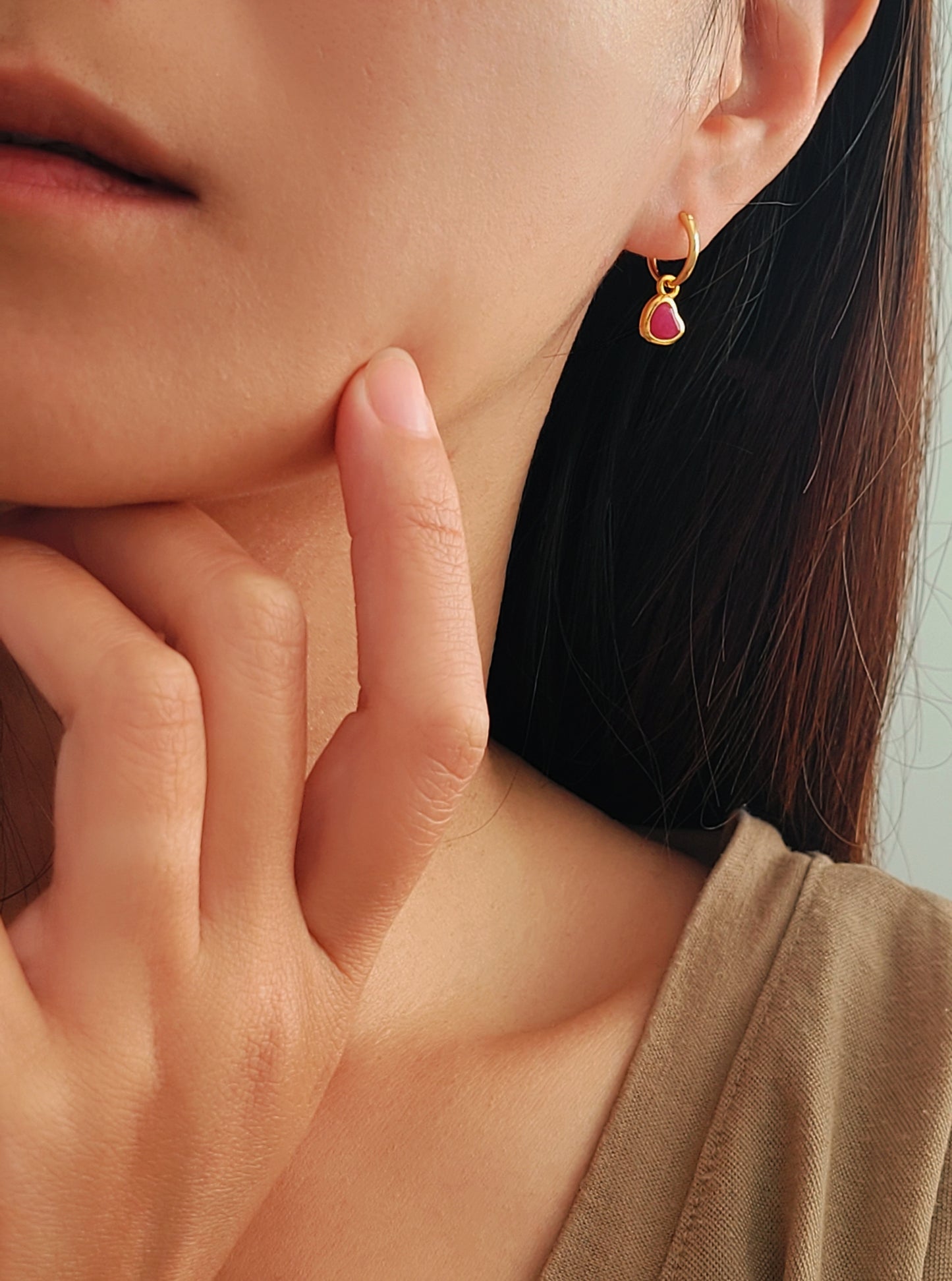 A woman wearing pink heart dangle earrings, dainty and delicate