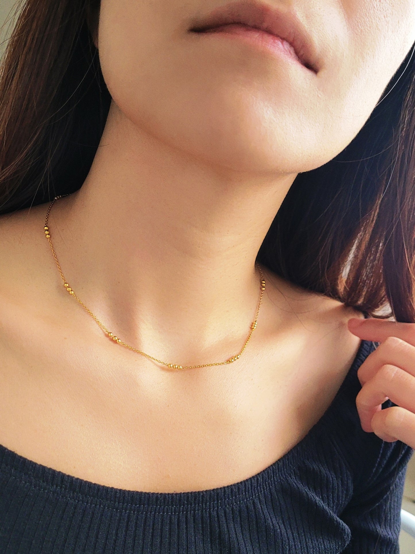 Close-up of a woman wearing a delicate 18ct gold vermeil triple ball necklace, showcasing its minimalist design with small gold beads spaced along a fine chain.