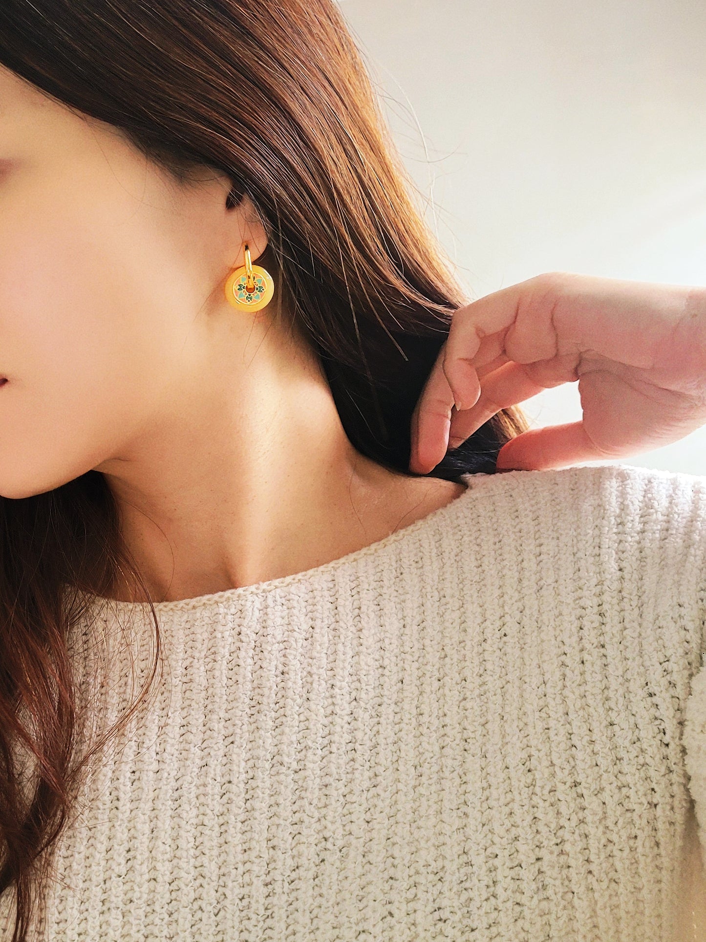 Close-up of a woman wearing vintage tile pattern inspired gold hoop earrings with floral detailing.