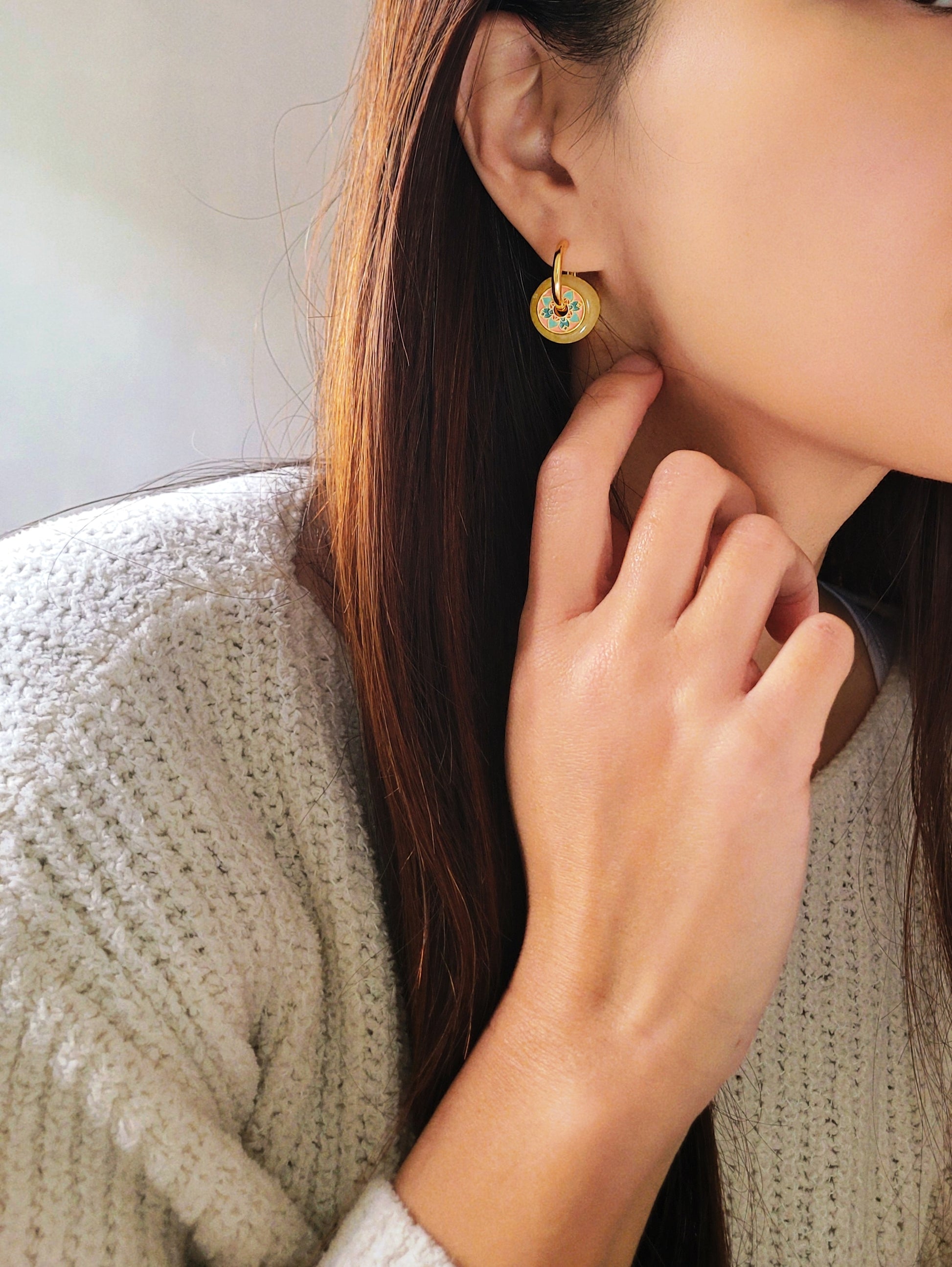Close-up of a woman wearing vintage tile pattern inspired gold hoop earrings with floral detailing.