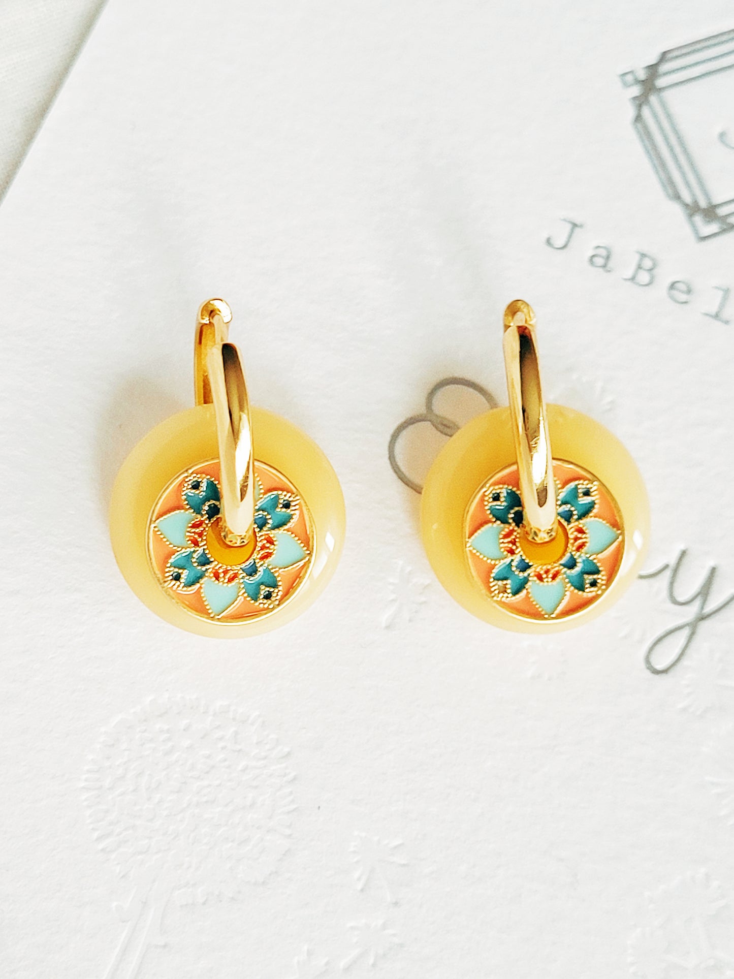 Close-up of vintage tile-pattern-inspired gold hoop earrings with floral detailing, displayed on a white background.