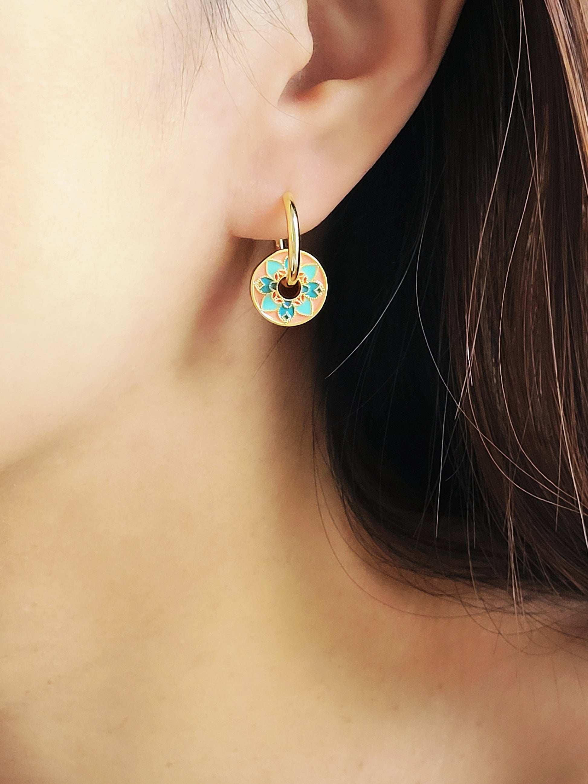 Close-up of a woman wearing vintage tile pattern inspired gold hoop earrings with floral detailing.