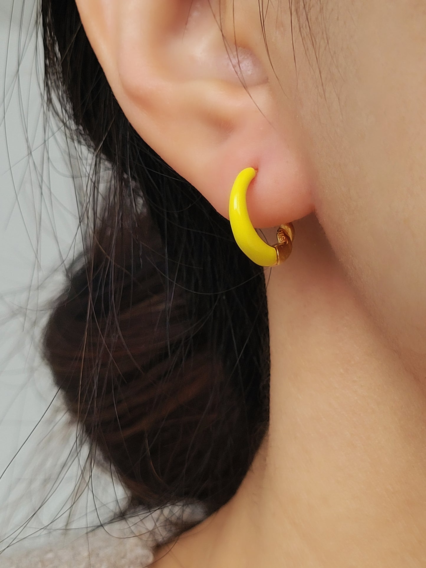 Model wearing small yellow and gold enamel hoop earrings, showcasing their elegant and lightweight design.