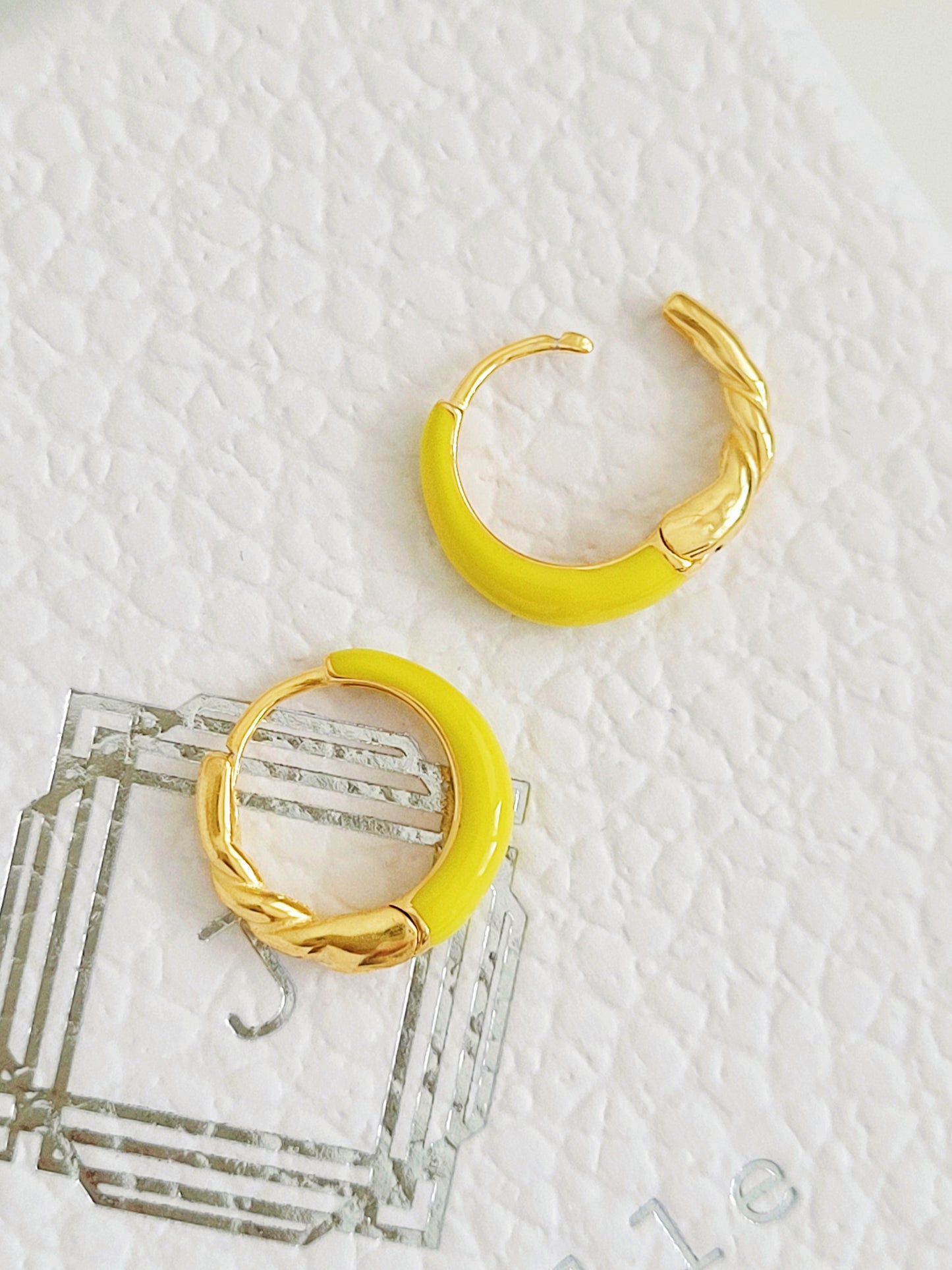 Gold hoop earrings with yellow enamel and gold accents on a textured white surface