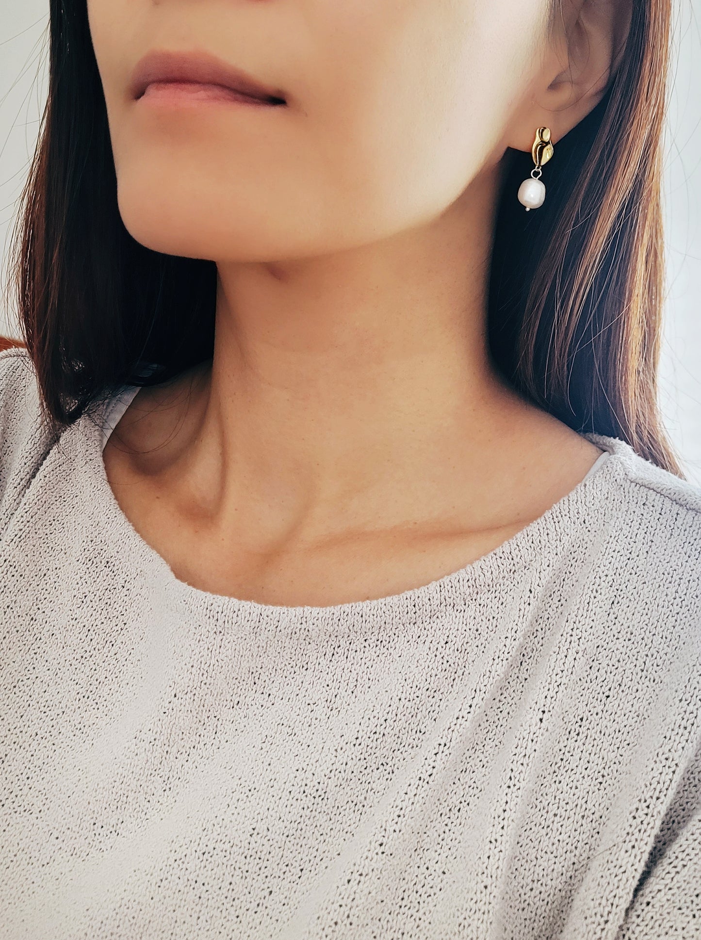 Gold earrings with a dangling baroque pearl drop, worn by a woman.