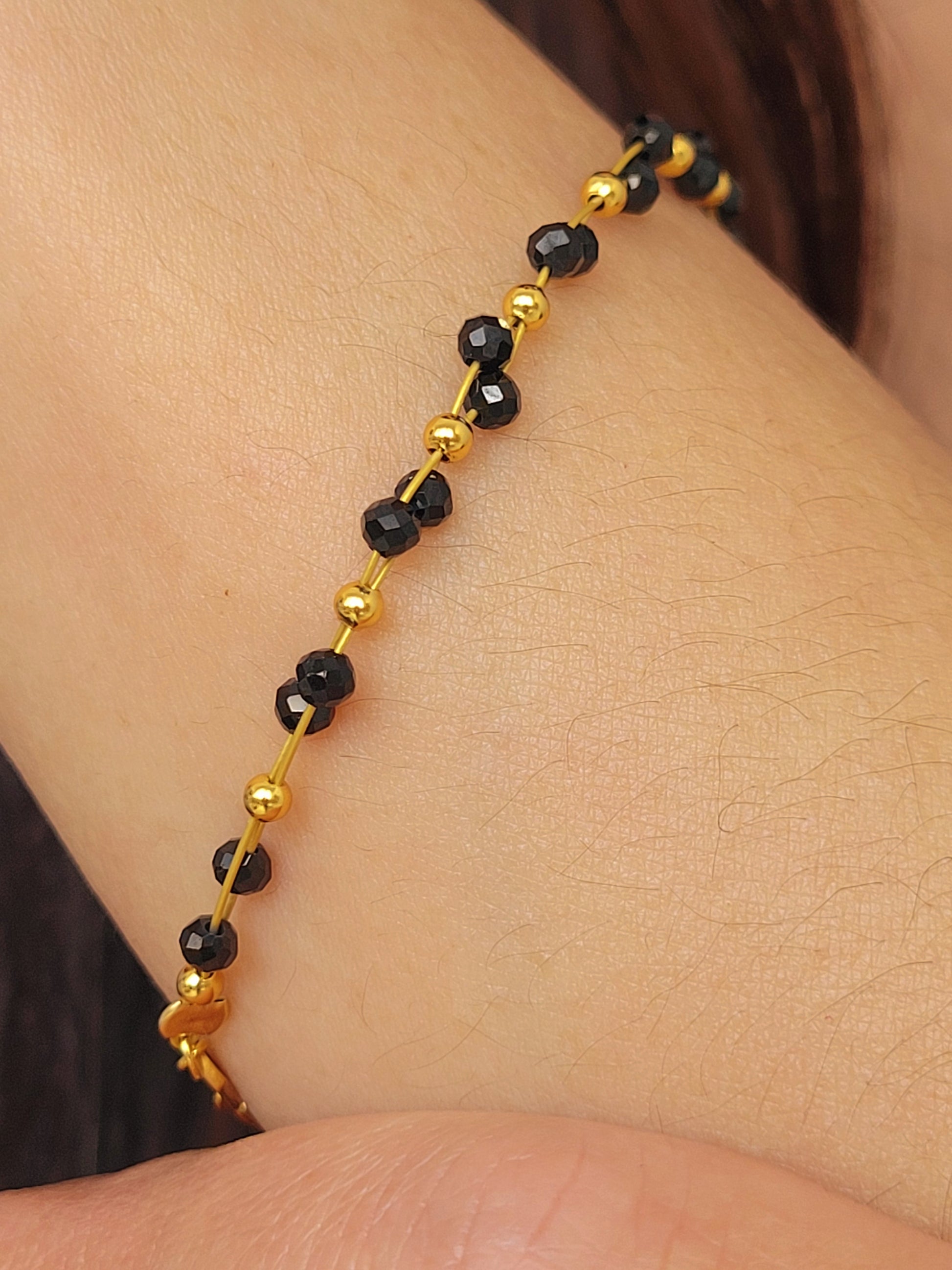 Close-up of a black spinel beaded bangle bracelet with 22k gold accents, styled for minimalist everyday wear. Handmade in natural gemstone and gold plated sterling silver premium materials, perfect gift for anniversary, birthday or self care.