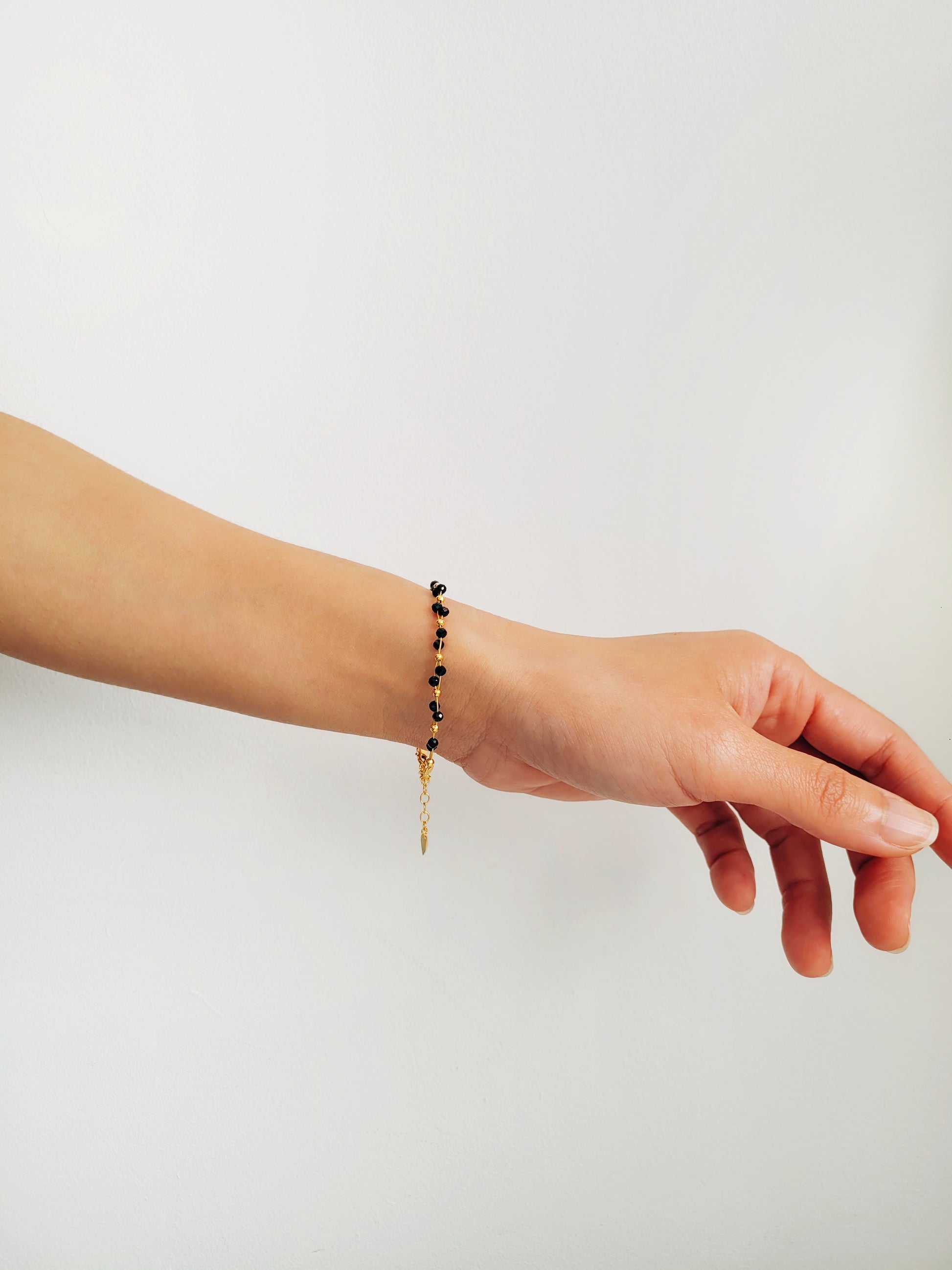 Close-up of a black spinel beaded bangle bracelet with 22k gold accents, styled for minimalist everyday wear. Handmade in natural gemstone and gold plated sterling silver premium materials, perfect gift for anniversary, birthday or self care.