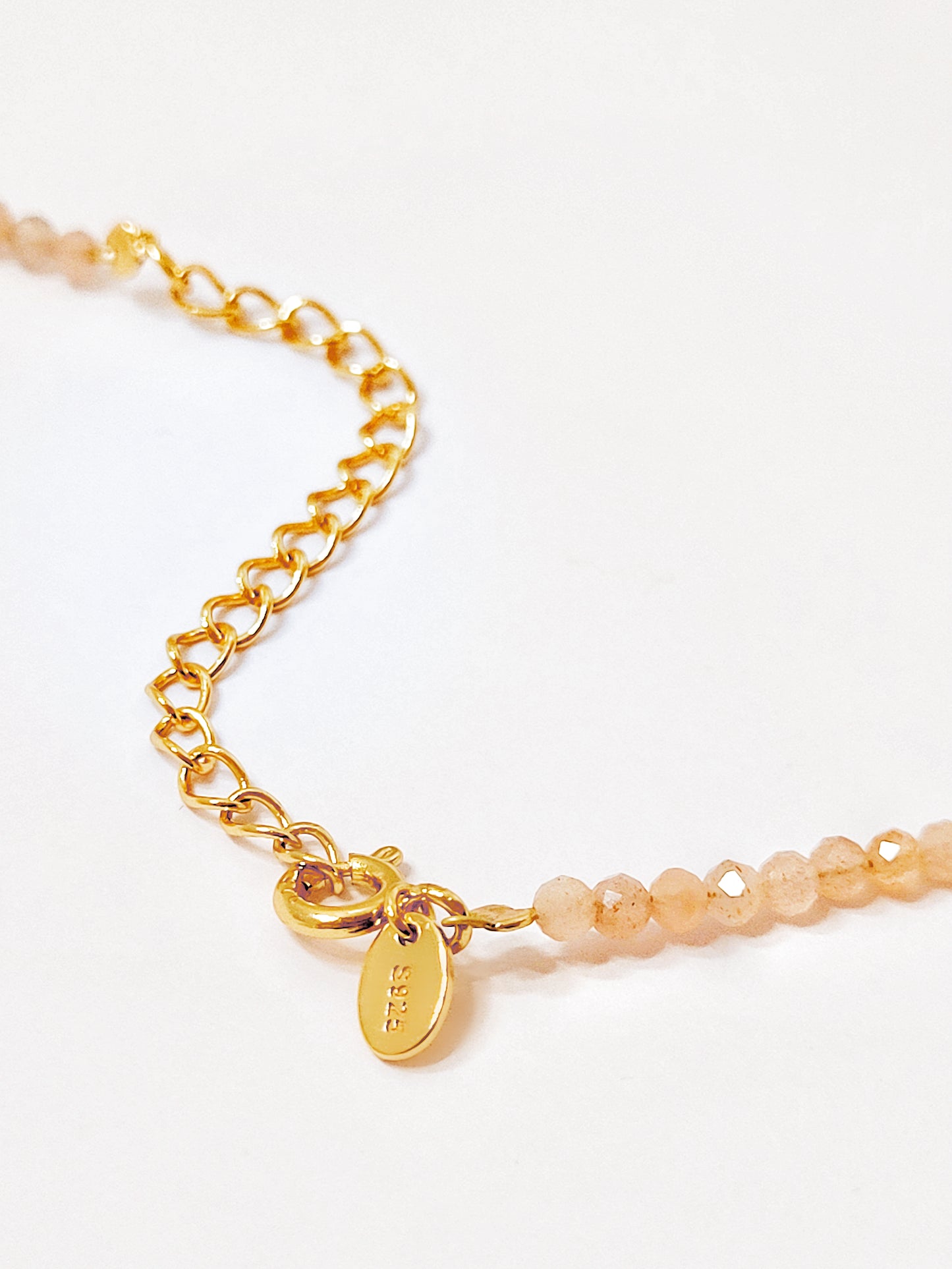 Close-up of the closure using spring ring on a natural sunstone gemstone choker necklace with S925 on a gold plated tag which means crafted in 925 sterling silver.