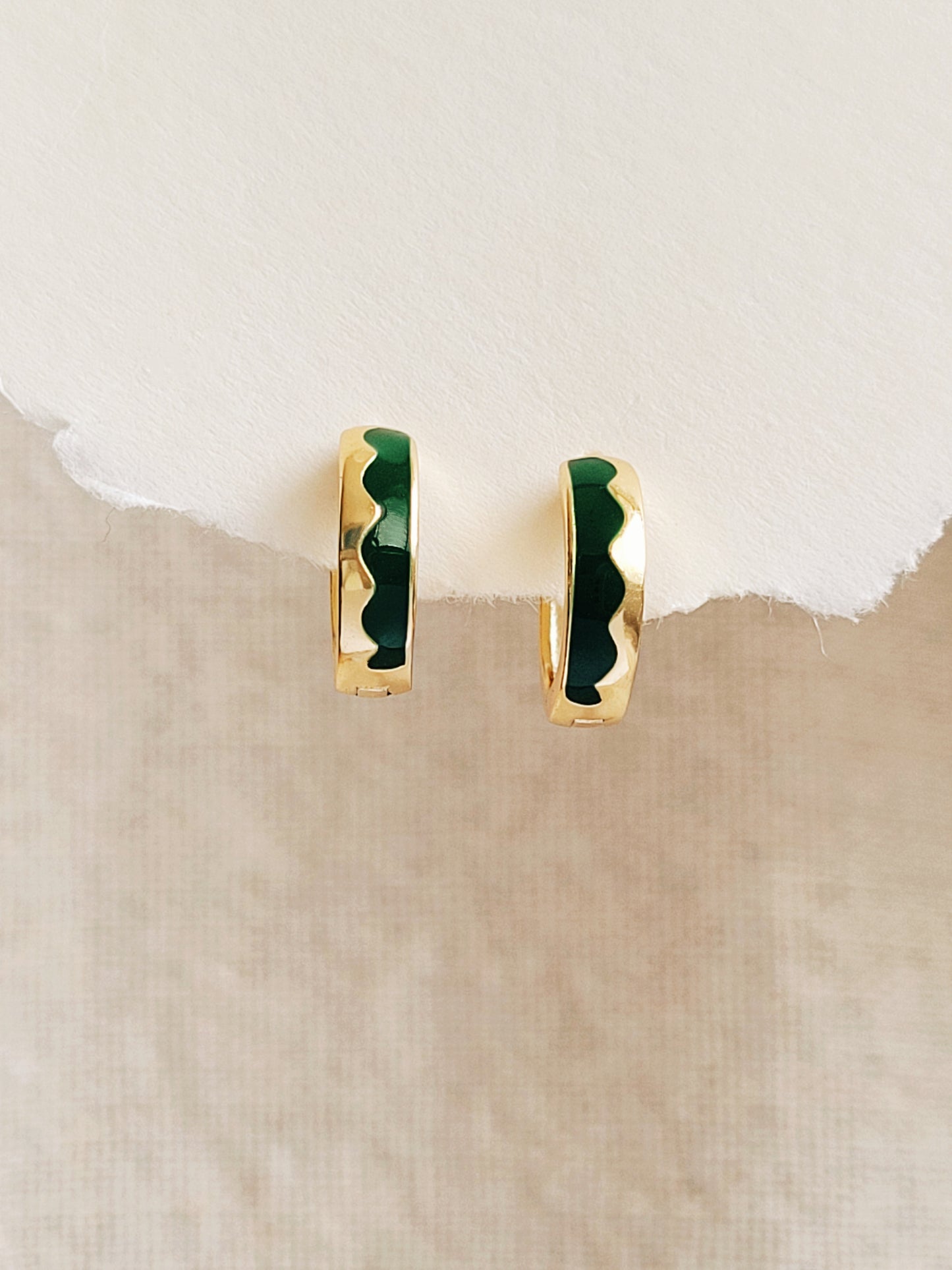 Gold hoop earrings with green enamel on a beige background