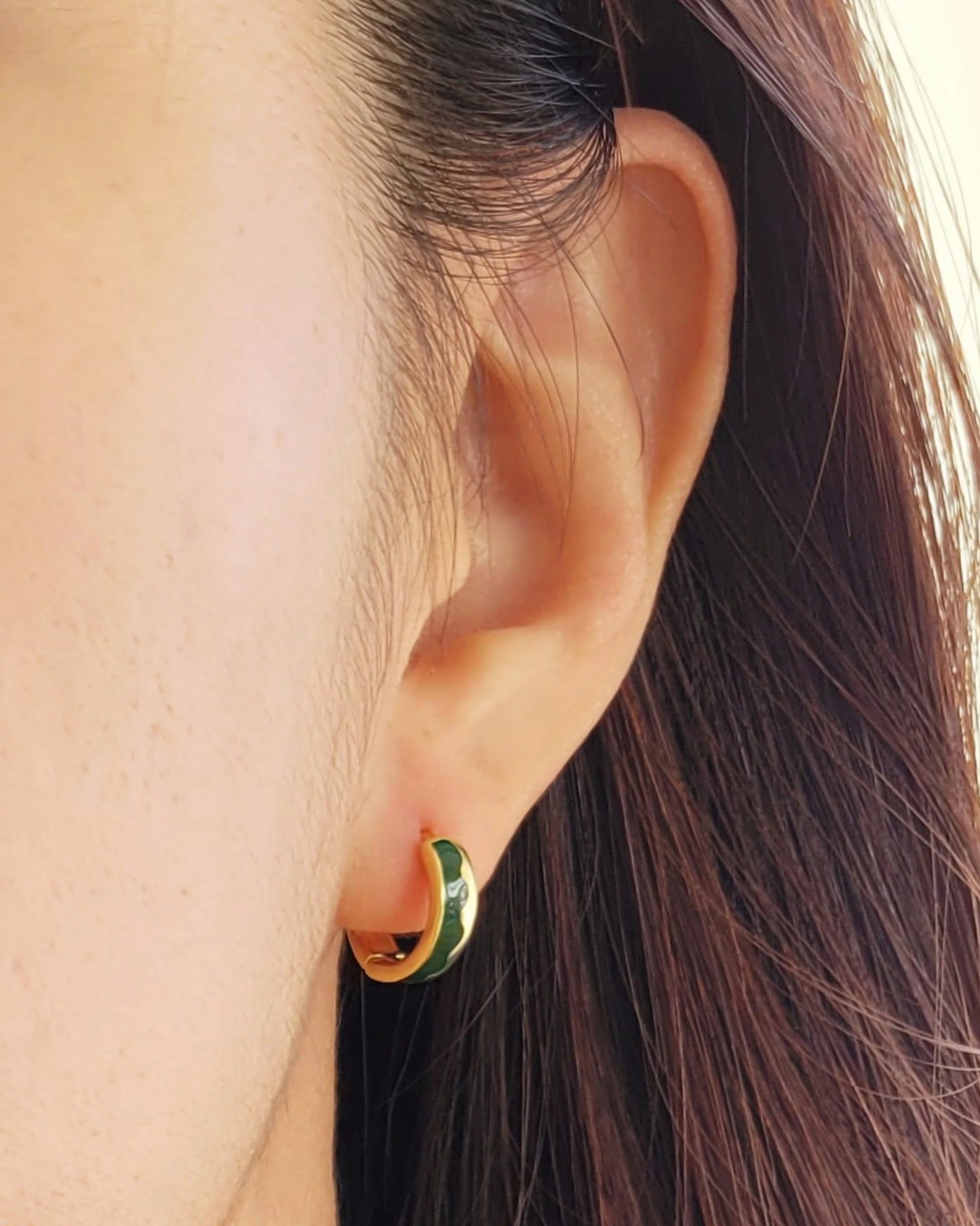 Close-up of an ear wearing a gold hoop earring with green enamel