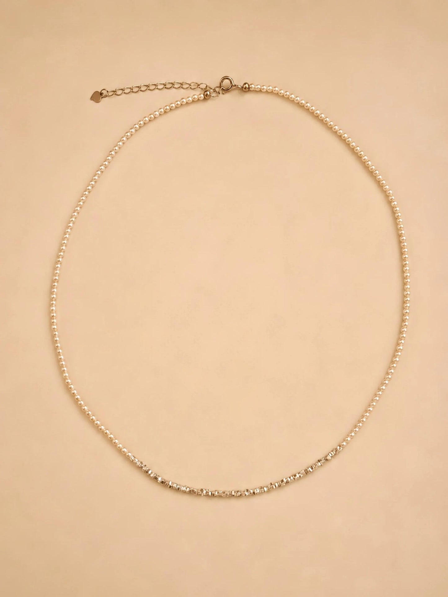 A dainty 2mm glass pearl choker necklaces displayed on a luxury beige color surface featuring textured sterling silver nugget beads.