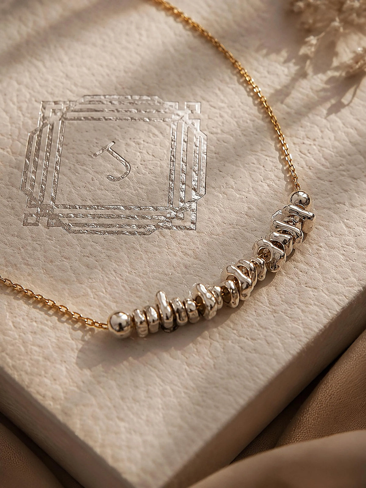 Silver beaded bracelet on gold chain displayed on a textured beige surface