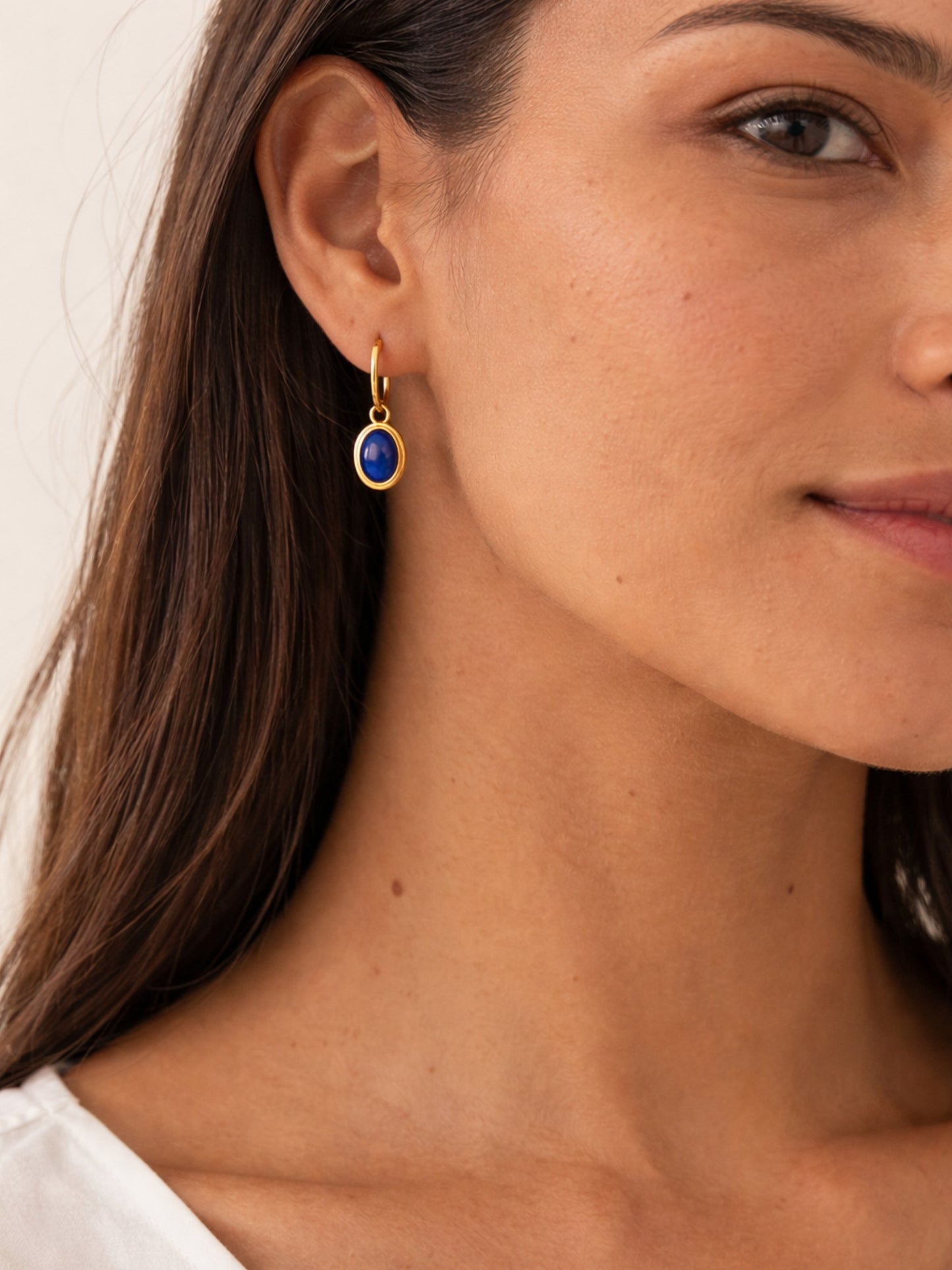 Close-up of a woman wearing a 22k gold earring with a blue lapis lazuli gemstone.